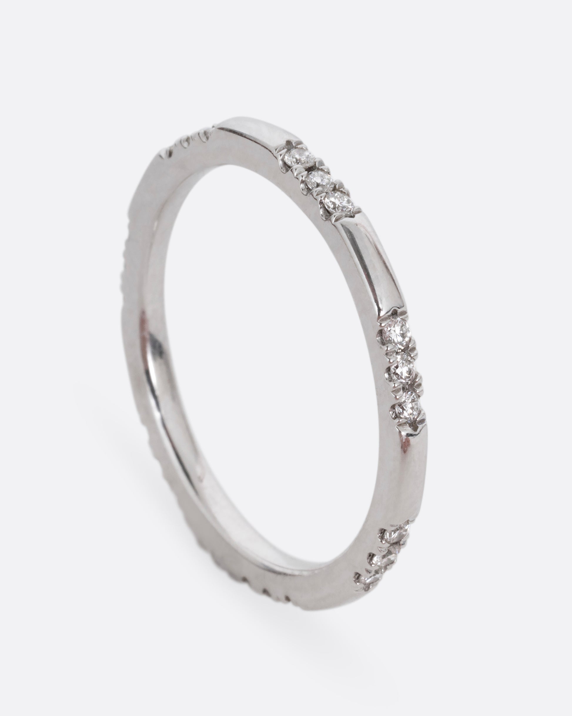 A platinum ring with stations of white diamonds. Shown standing up from the side.