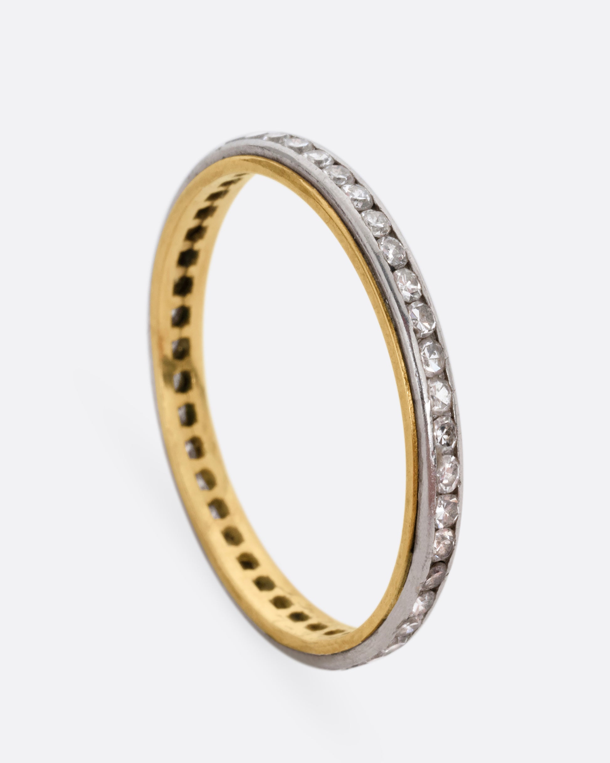 A platinum and yellow gold ring with channel set diamonds. Shown standing up from the side.