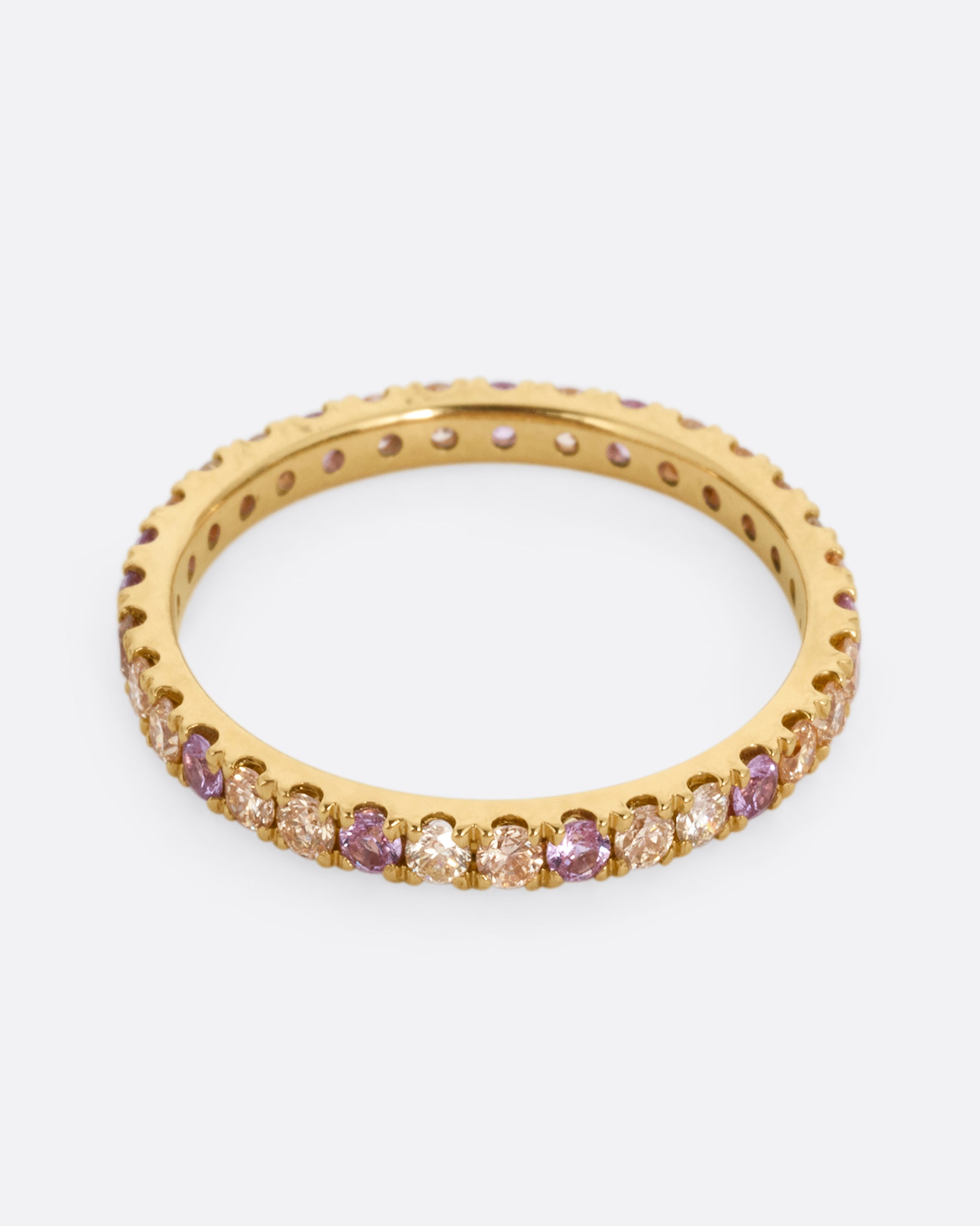 A yellow gold eternity band with peach and yellow diamonds and purple sapphires. Shown from the front.