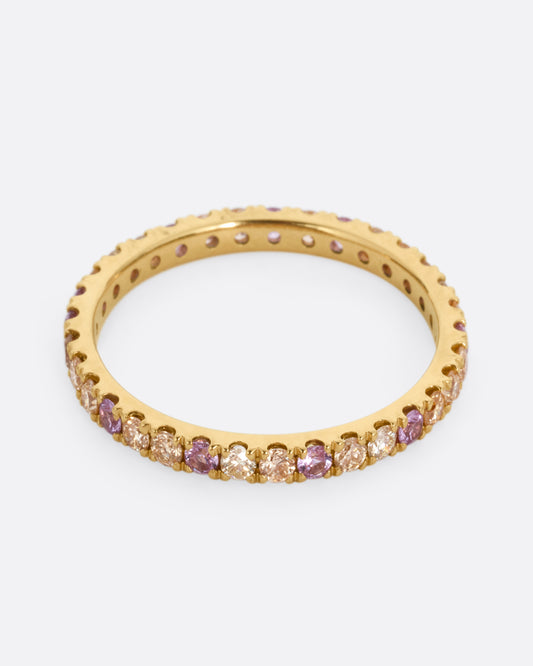A yellow gold eternity band with peach and yellow diamonds and purple sapphires. Shown from the front.