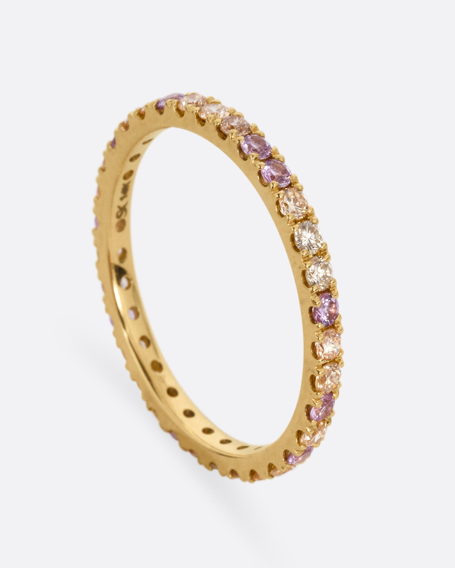 A yellow gold eternity band with peach and yellow diamonds and purple sapphires. Shown standing up from the front.