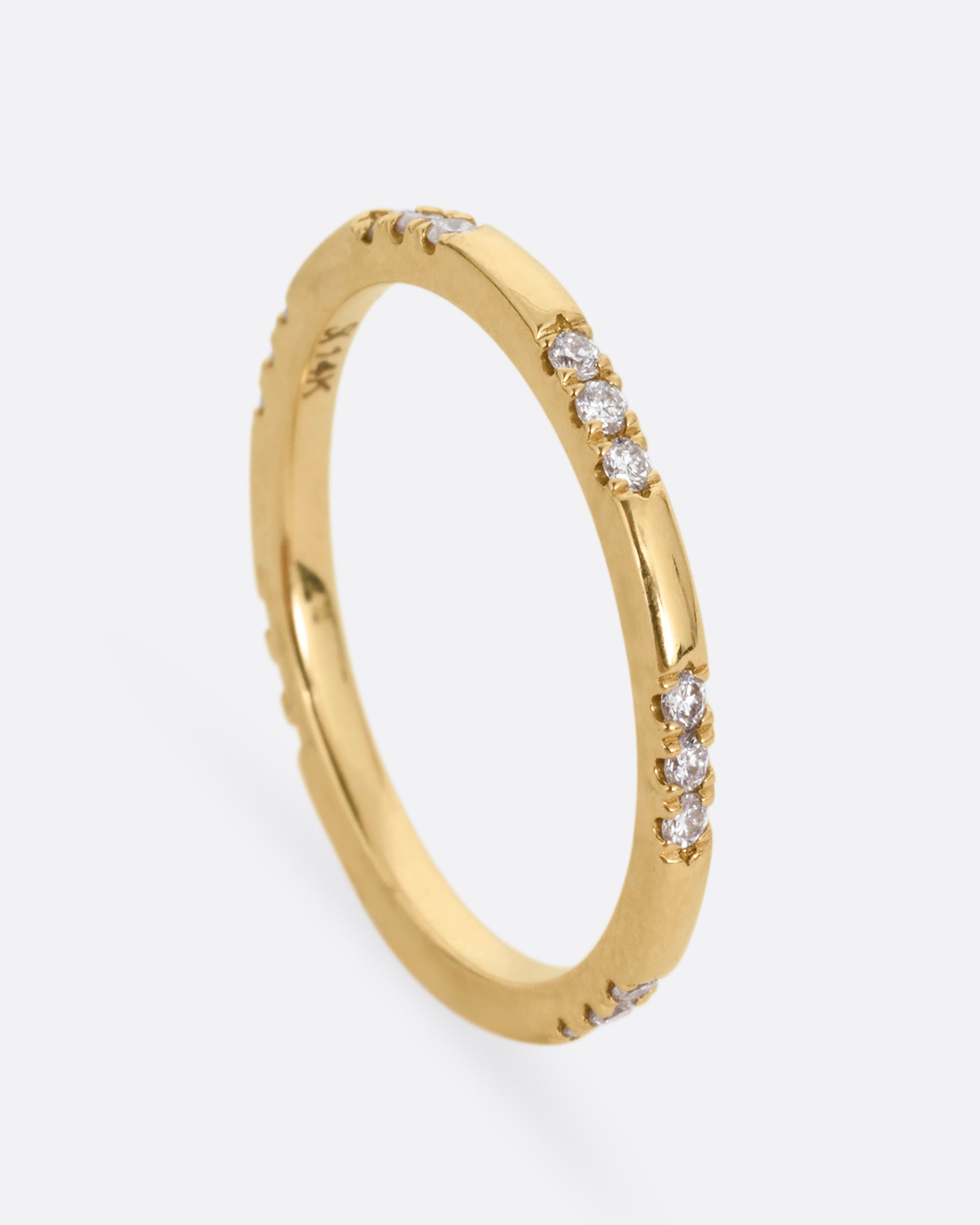 A yellow gold ring with stations of white diamonds. Shown standing up from the front.