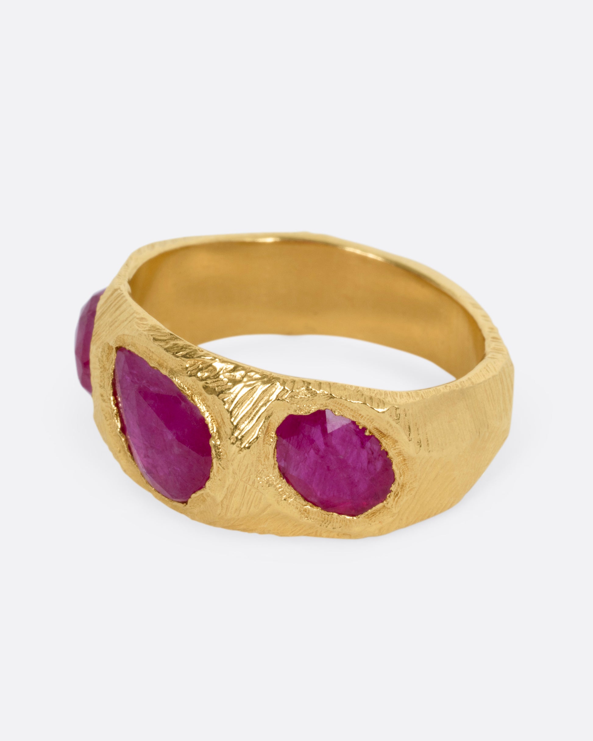 A yellow gold ring with three rubies, shown from the side.