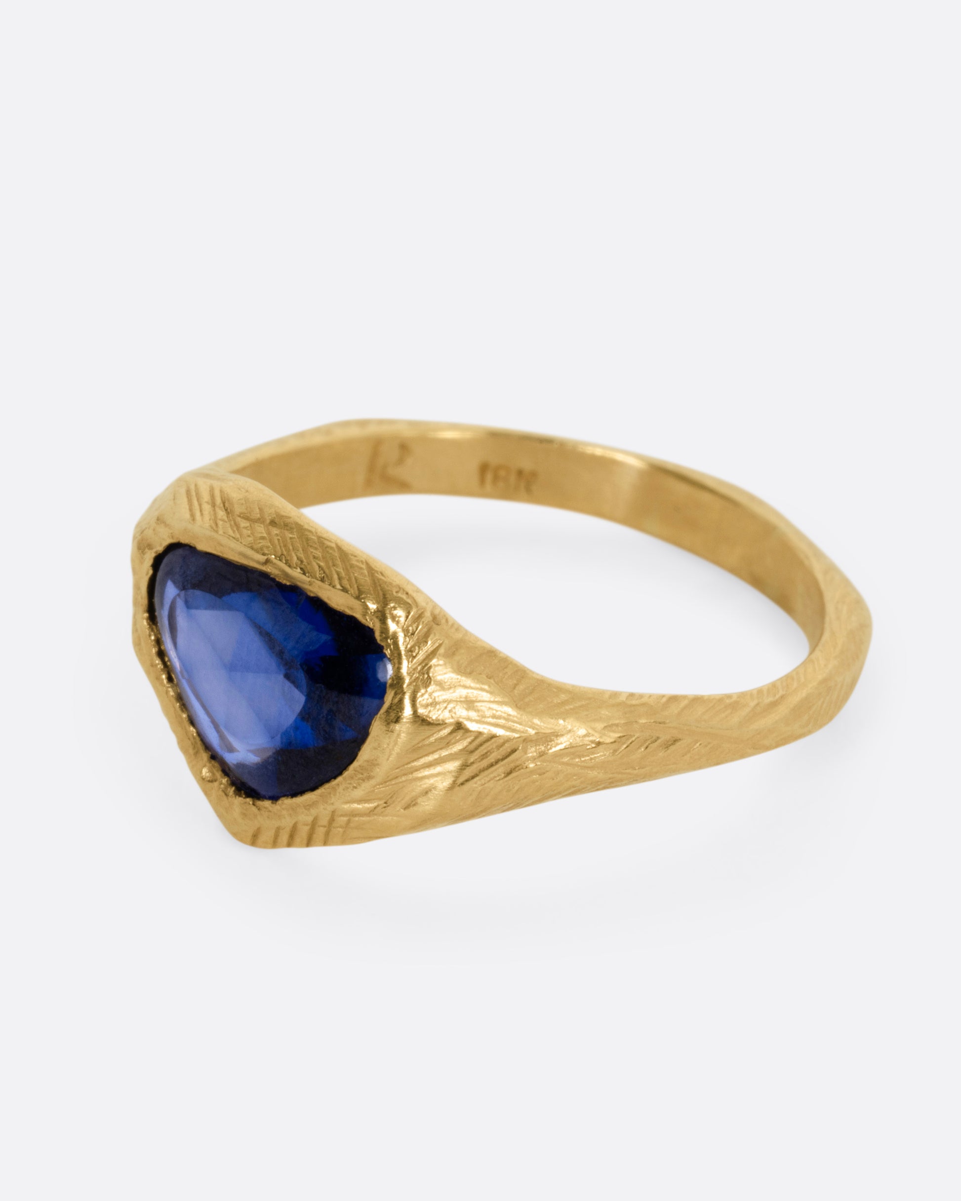 A yellow gold ring with a blue sapphire, shown from the side.