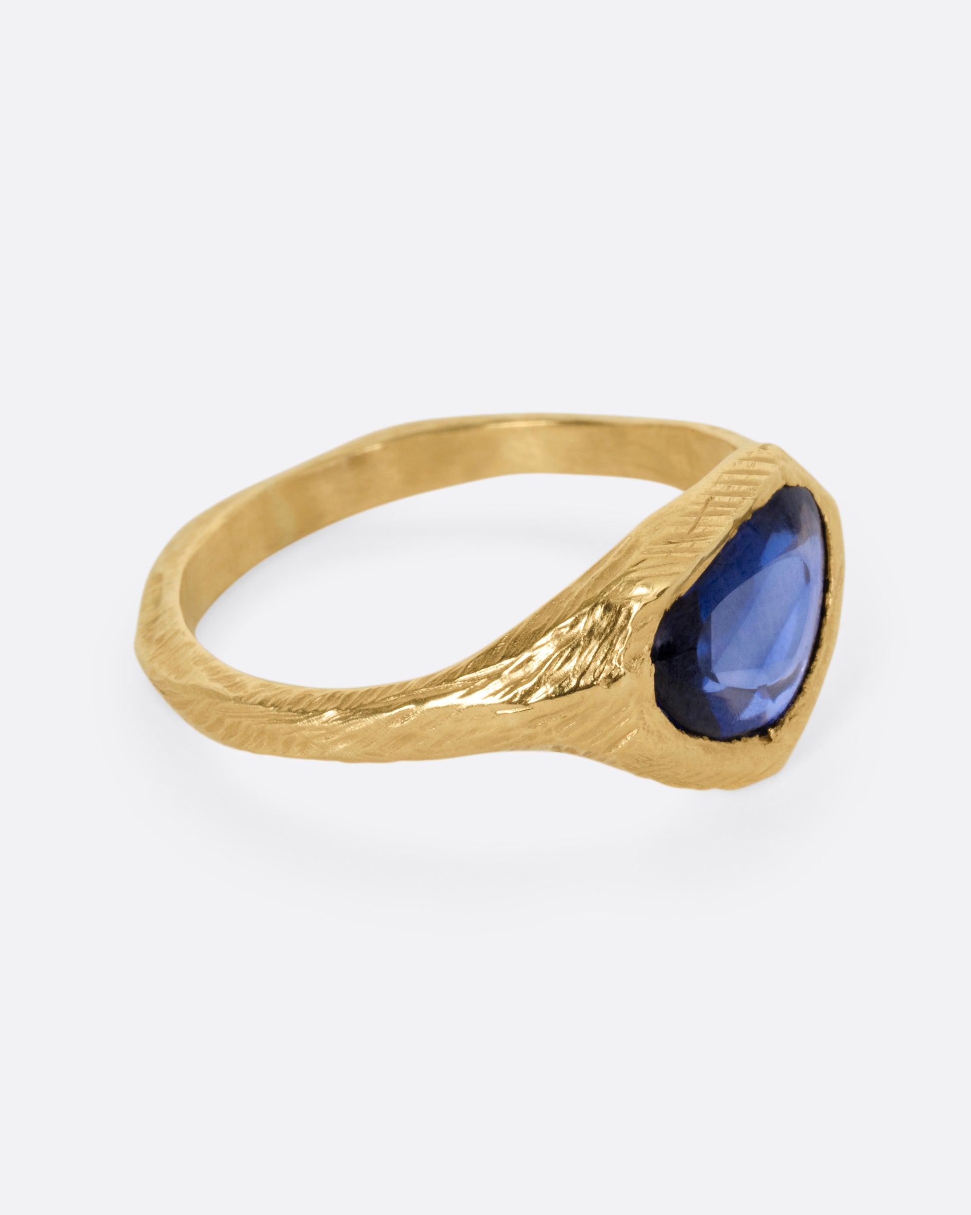 A yellow gold ring with a blue sapphire, shown from the side.