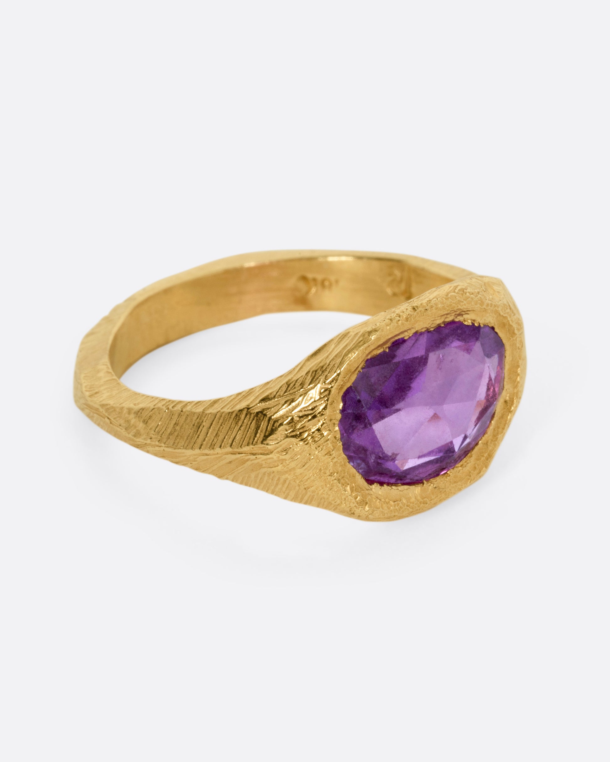 A yellow gold ring with a purple sapphire, shown from the side.