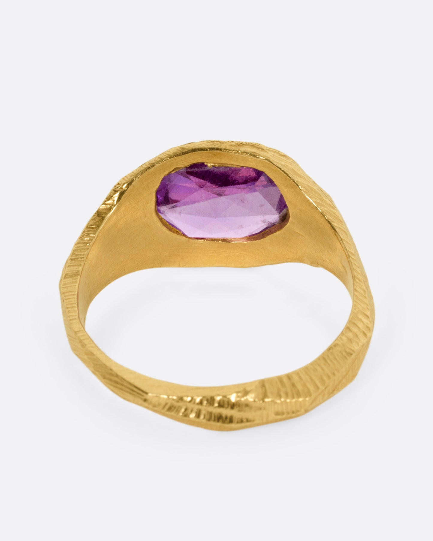 A yellow gold ring with a purple sapphire, shown from the back.