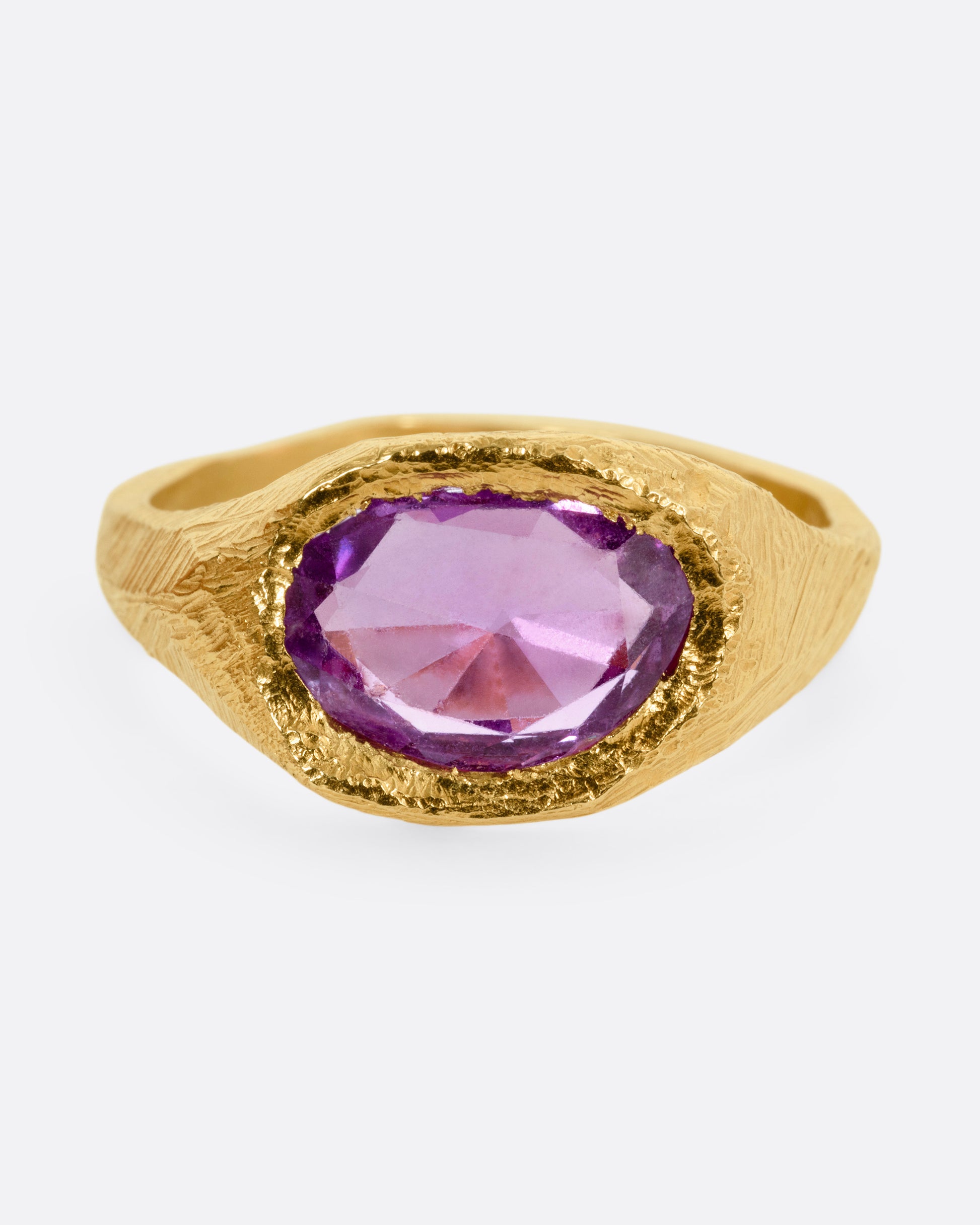 A yellow gold ring with a purple sapphire, shown from the front.
