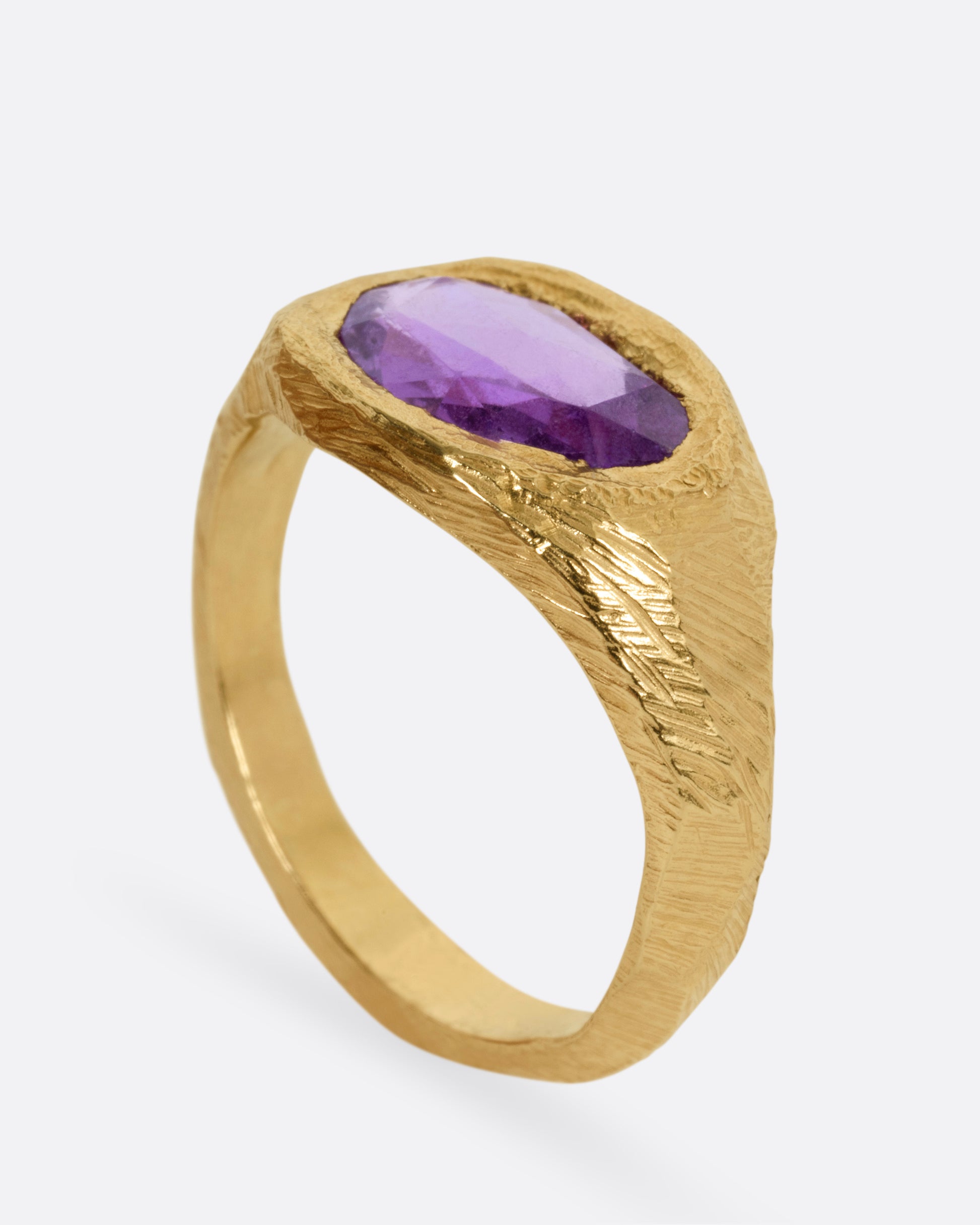 A yellow gold ring with a purple sapphire, shown from the side standing up.