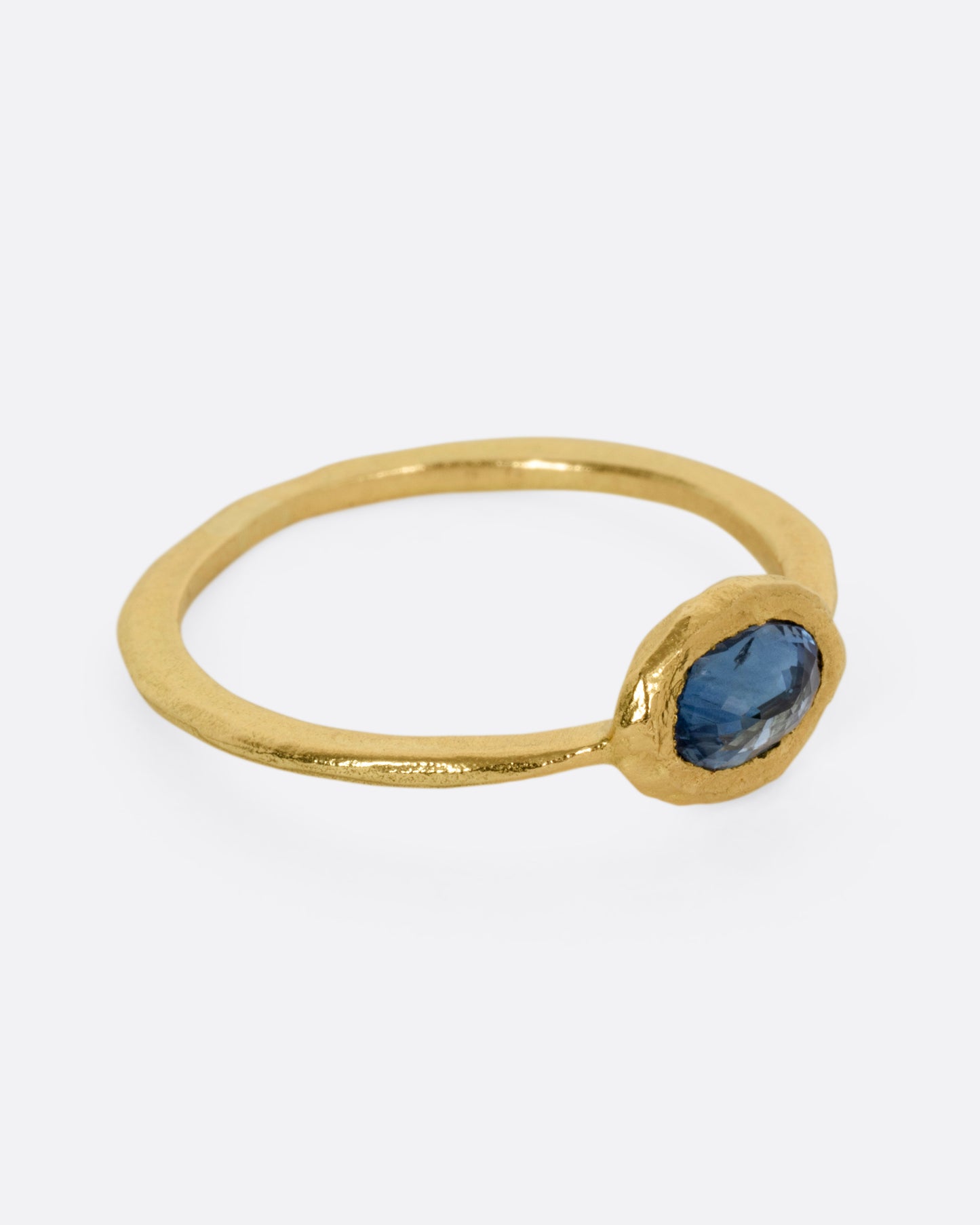 A yellow gold ring with a blue sapphire, shown from the side.