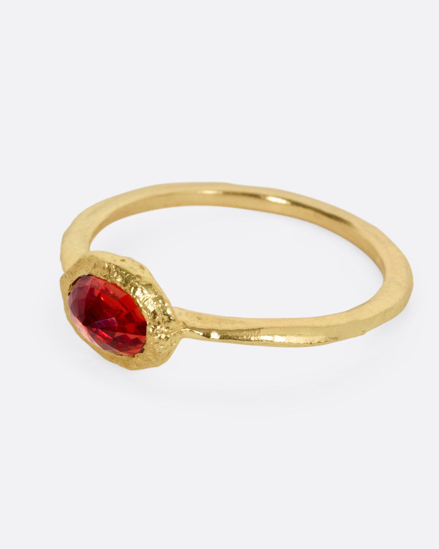 A yellow gold ring with a red sapphire, shown from the side.
