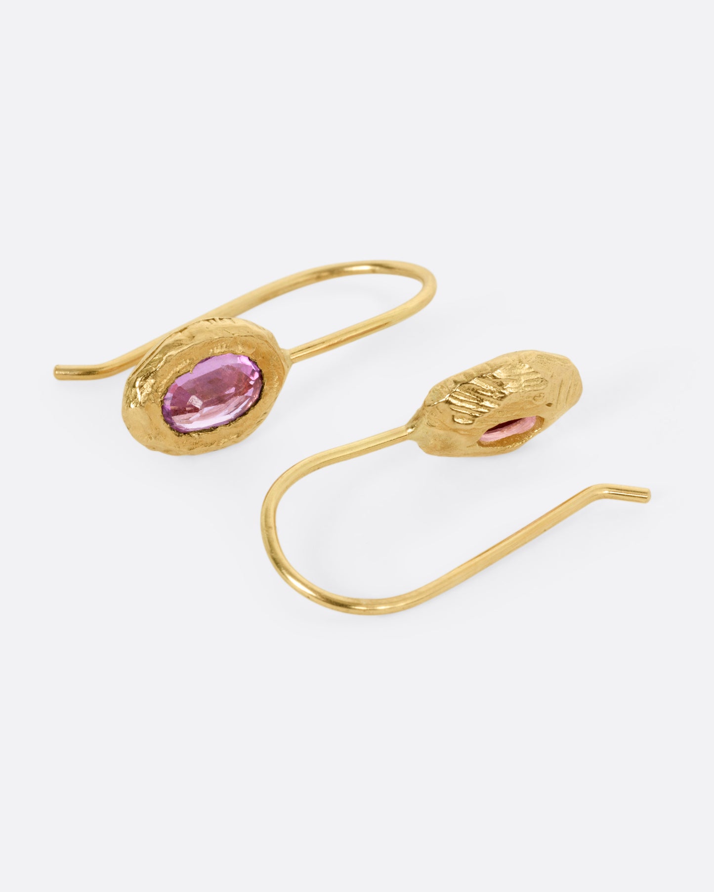 A pair of yellow gold earrings with pink sapphires, shown from the side.