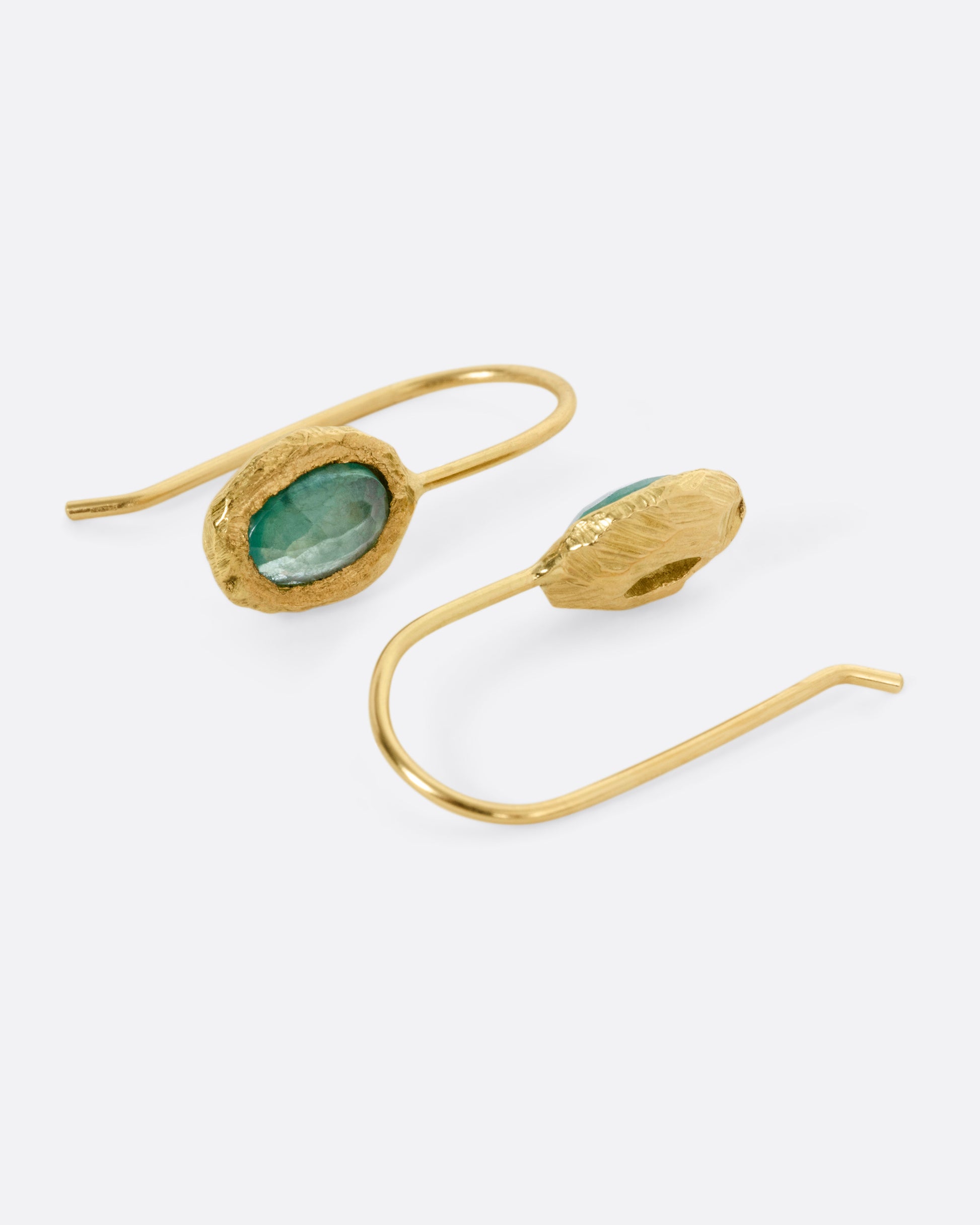 A pair of yellow gold hook earrings with emeralds, shown on their sides.