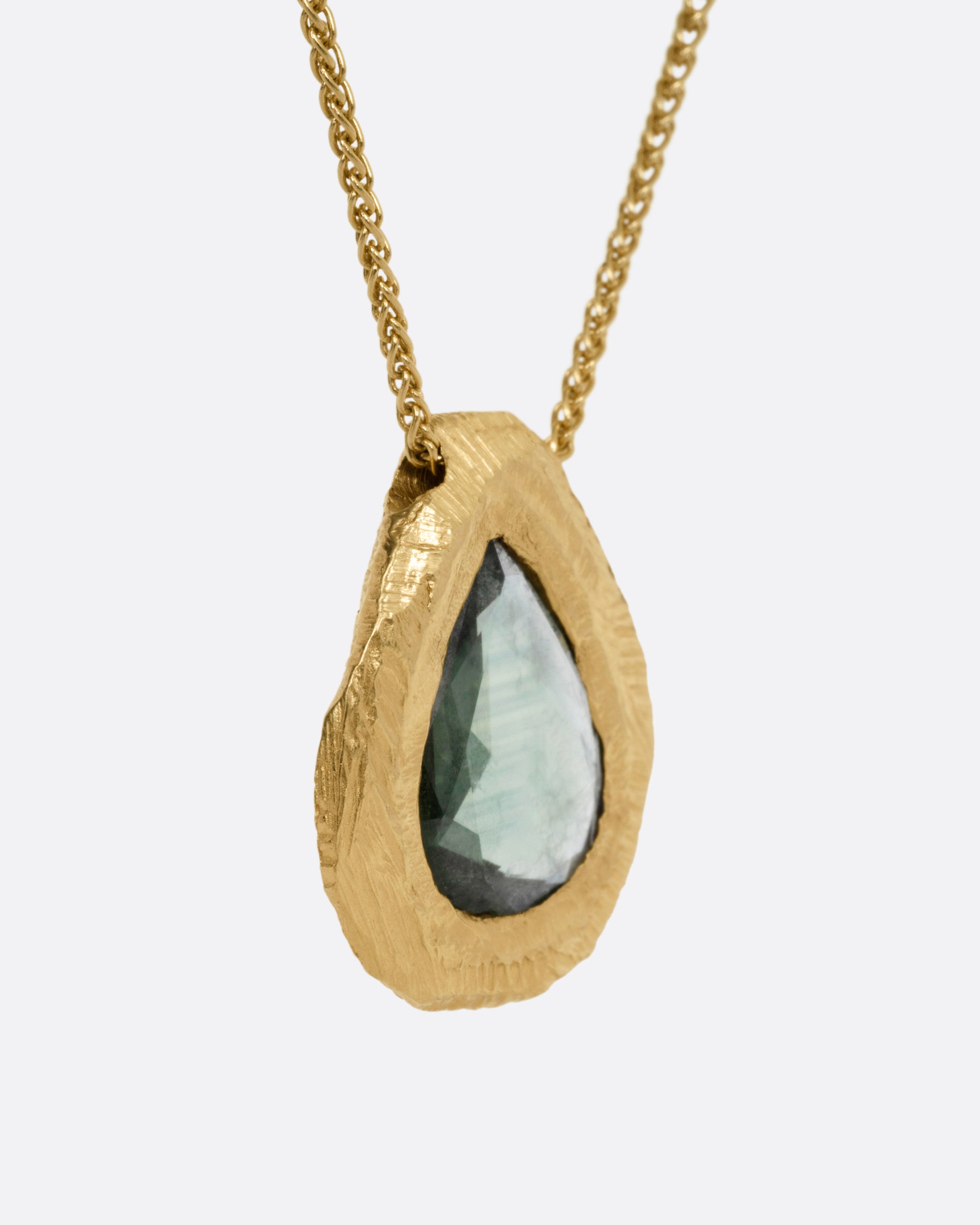 A yellow gold necklace with a green rose cut sapphire pendant, shown from the side.