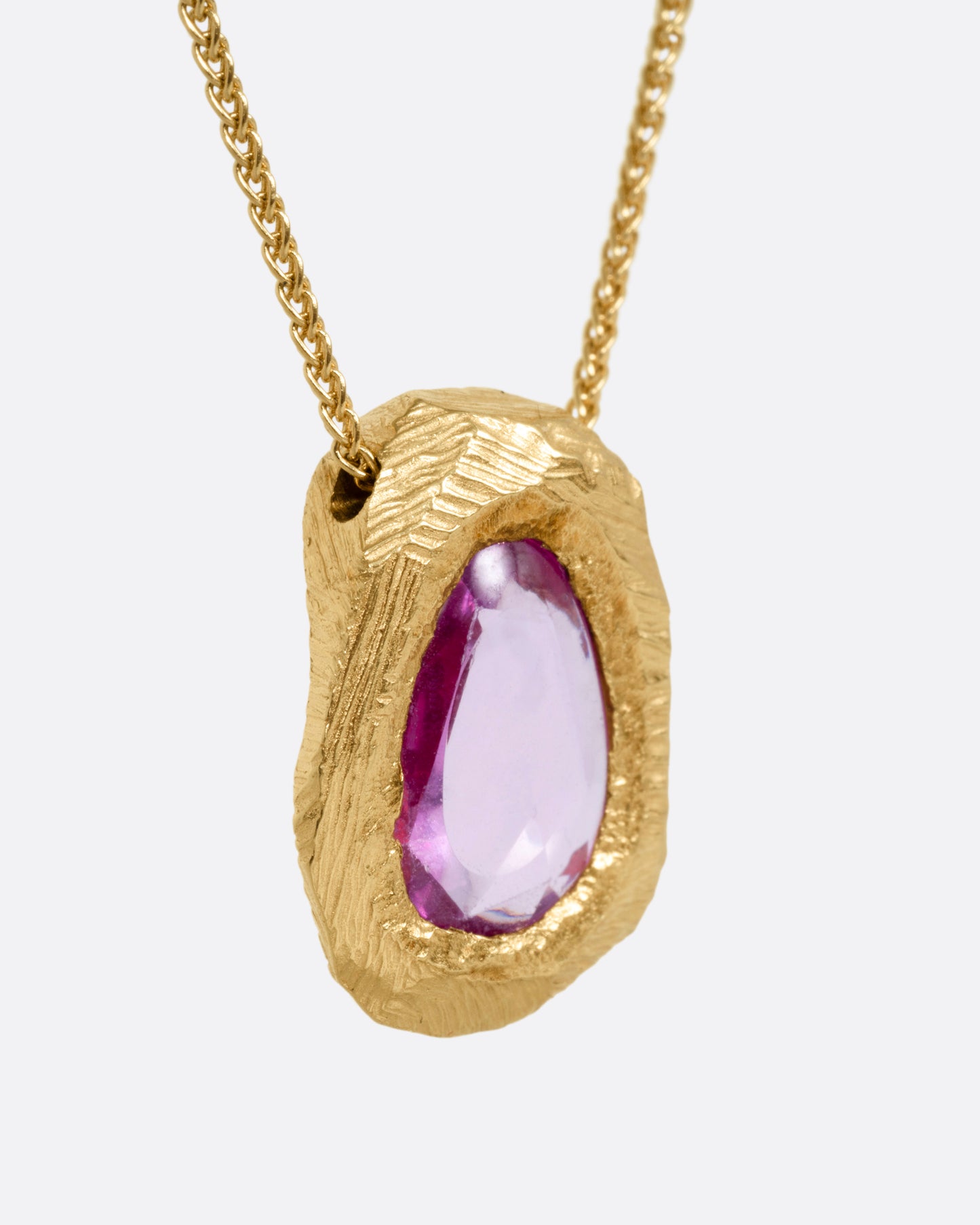 A yellow gold necklace with a pink sapphire pendant, shown from the side.