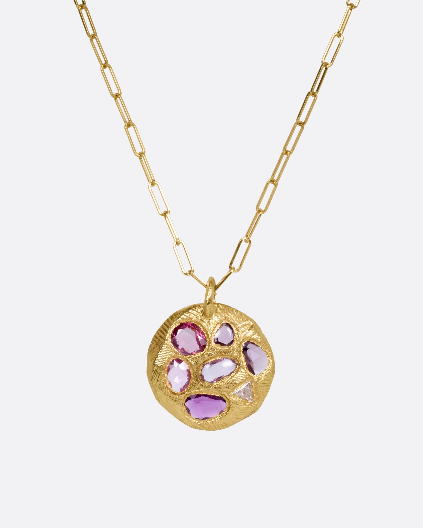 A yellow gold necklace with a circular pendant with pink sapphires and one trillion cut diamond, shown from the front.