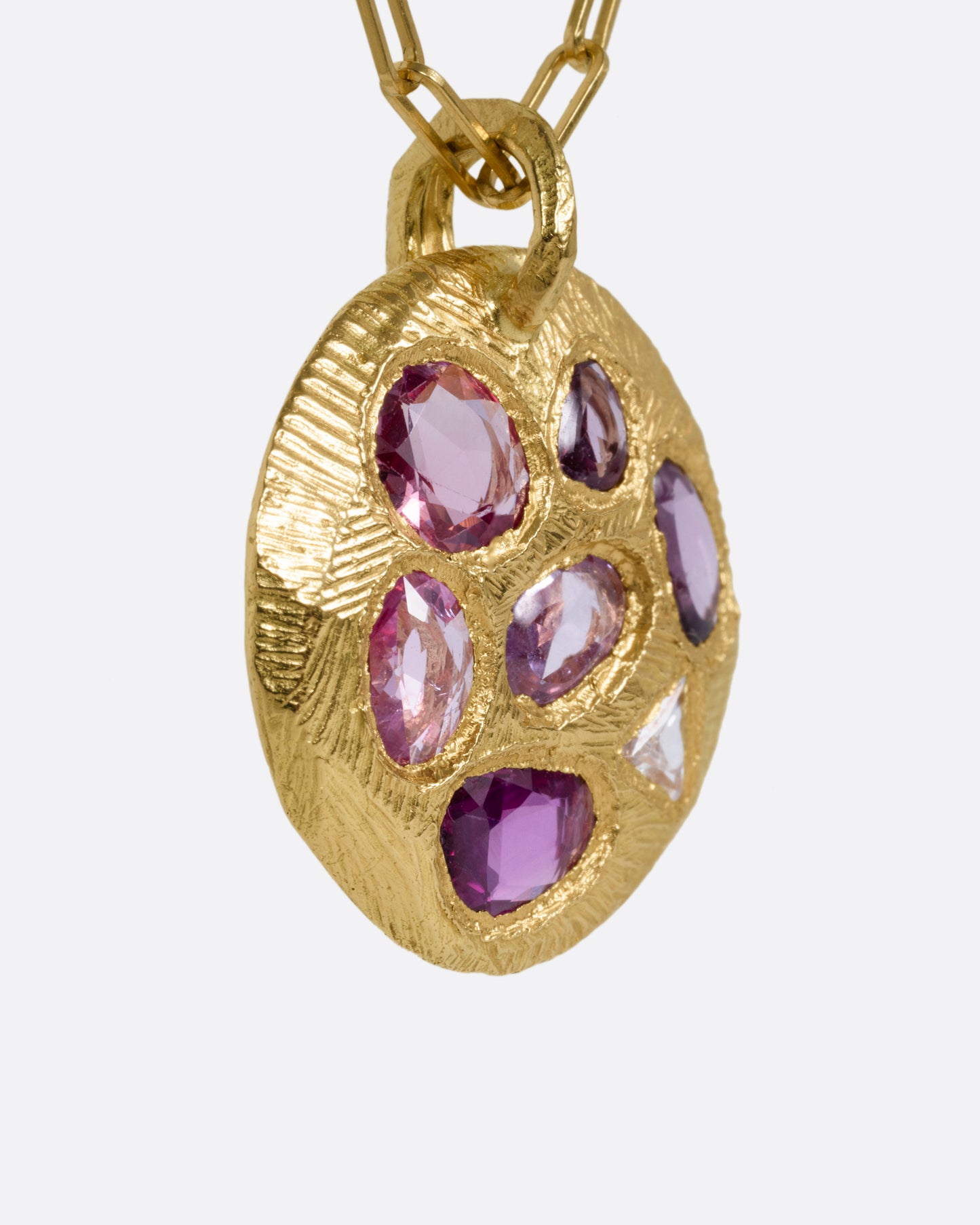 A yellow gold necklace with a circular pendant with pink sapphires and one trillion cut diamond, shown from the side.