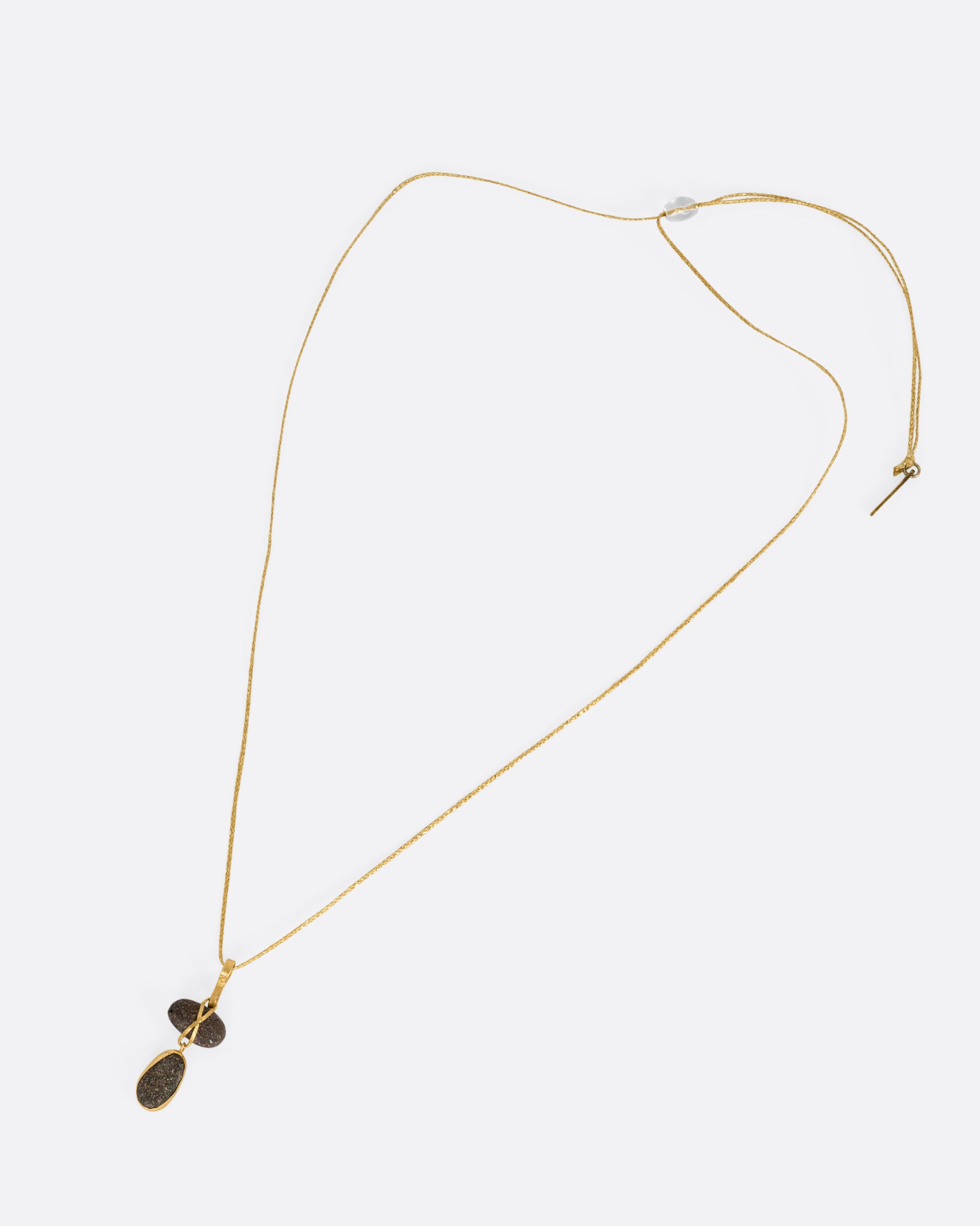 A yellow gold pendant with two Japanese river pebbles on a cord, shown from the front.