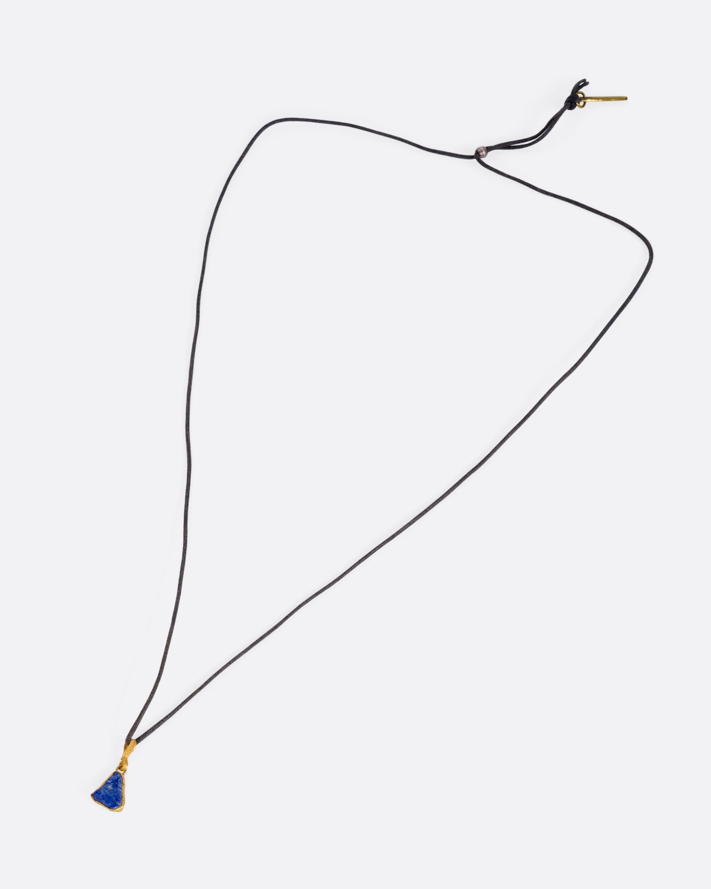 A yellow gold pendant with a raw triangular lapis on a black cord, shown from the front.