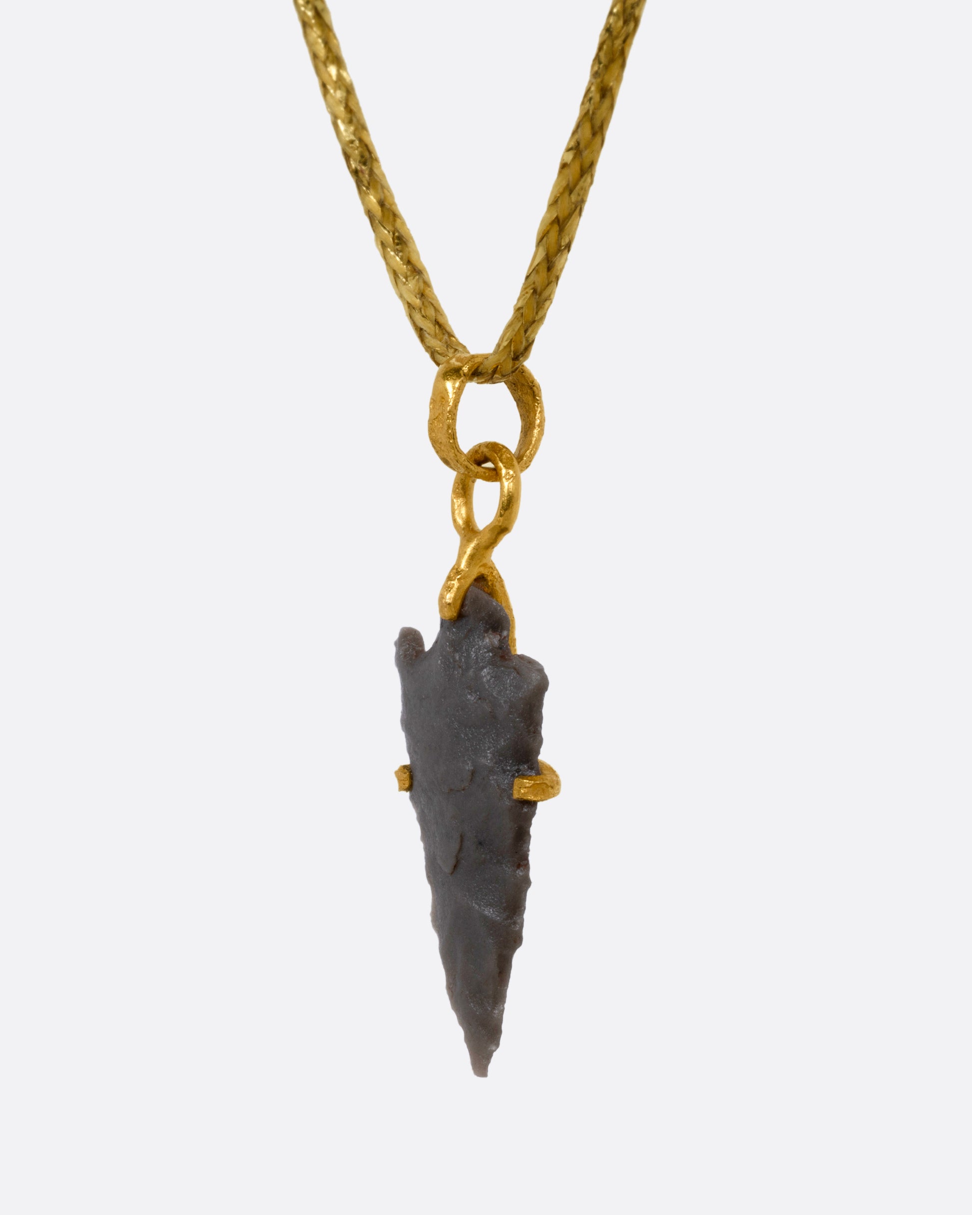 A yellow gold pendant with an ancient arrowhead on a cord, shown from the back.