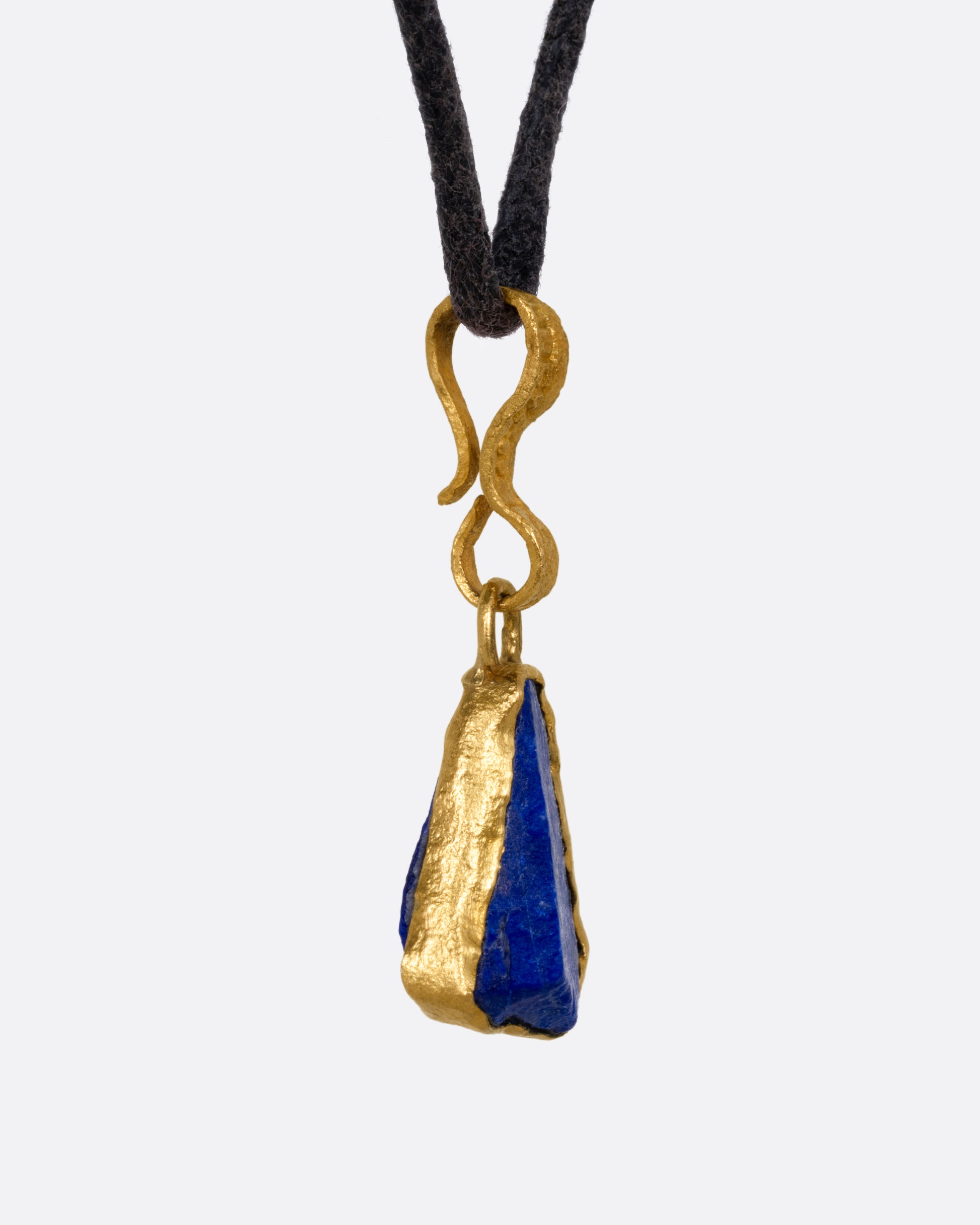 A yellow gold pendant with a raw triangular lapis on a black cord, shown from the side.