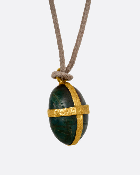 A Japanese river pebble pendant wrapped in yellow gold and hanging from a cord, shown from the side.