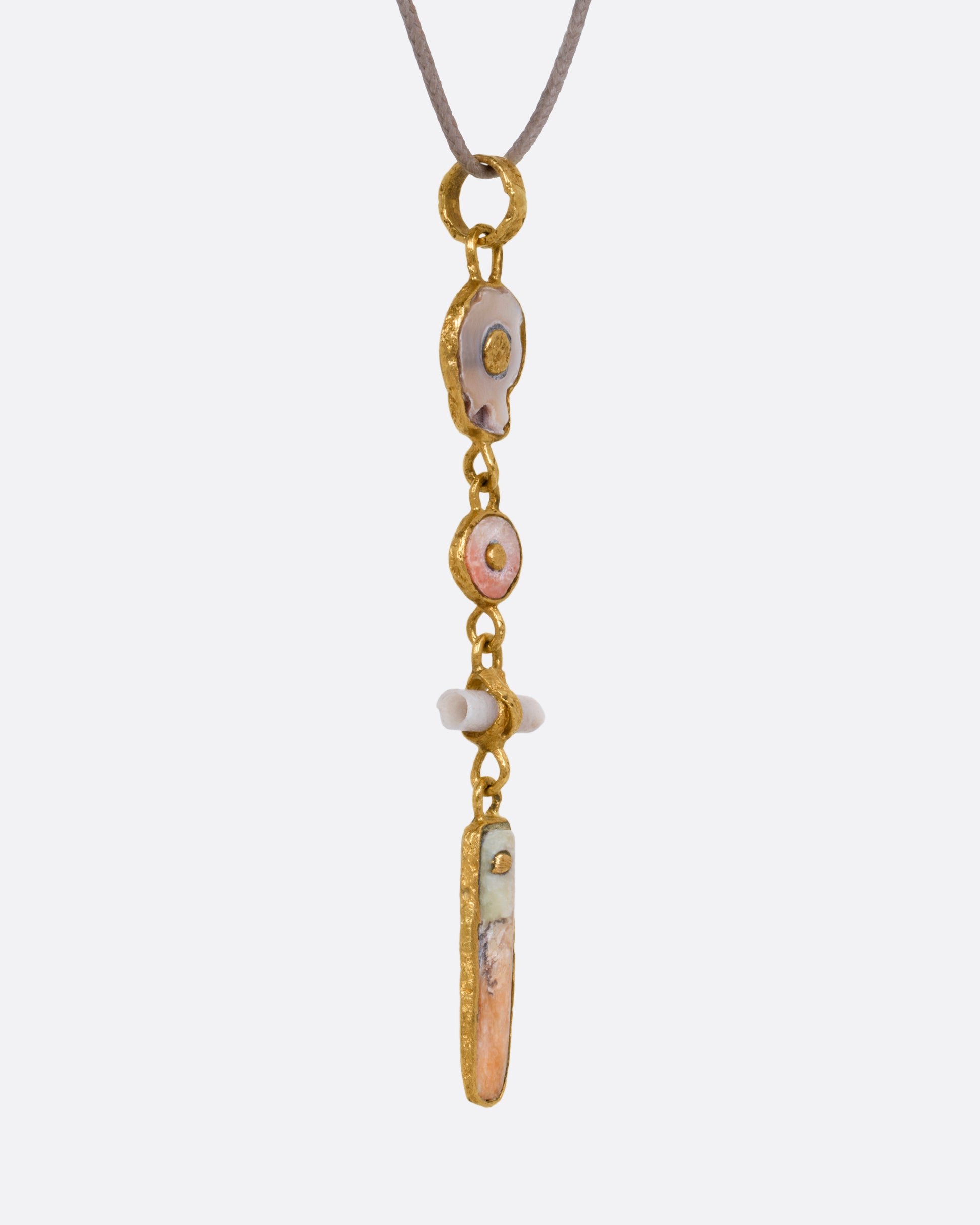 A yellow gold pendant with four gold wrapped pieces on a cord, shown from the side.