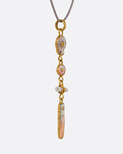 A yellow gold pendant with four gold wrapped pieces on a cord, shown from the side.
