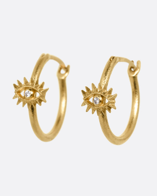 A pair of yellow gold hoop earrings with diamond studded eyes with dramatic lashes. Shown from the side.