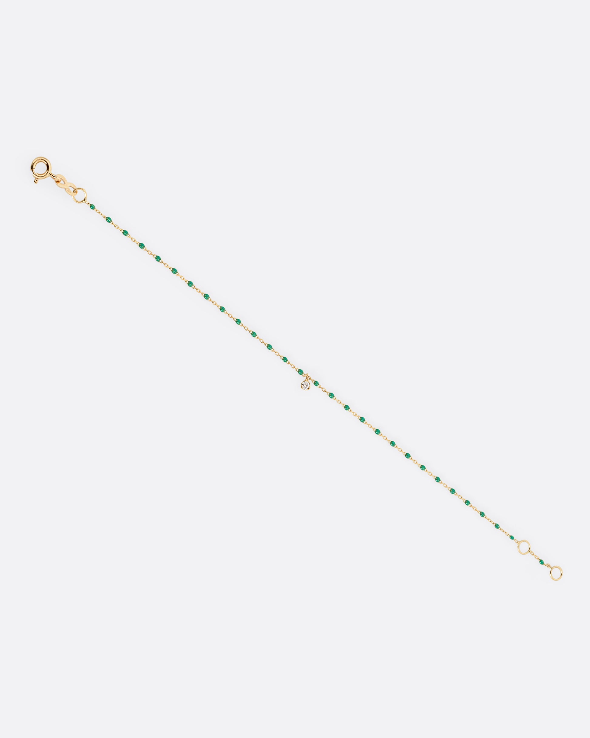 A yellow gold cable chain bracelet with green resin droplets throughout and a single diamond charm. Shown from the front.