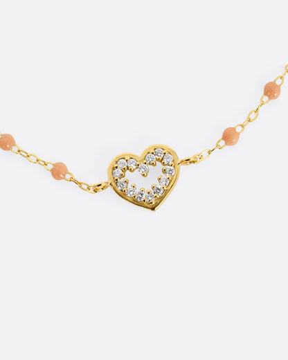 A close up of a yellow gold cable chain bracelet with a diamond lined heart charm and caramel brown resin droplets throughout.