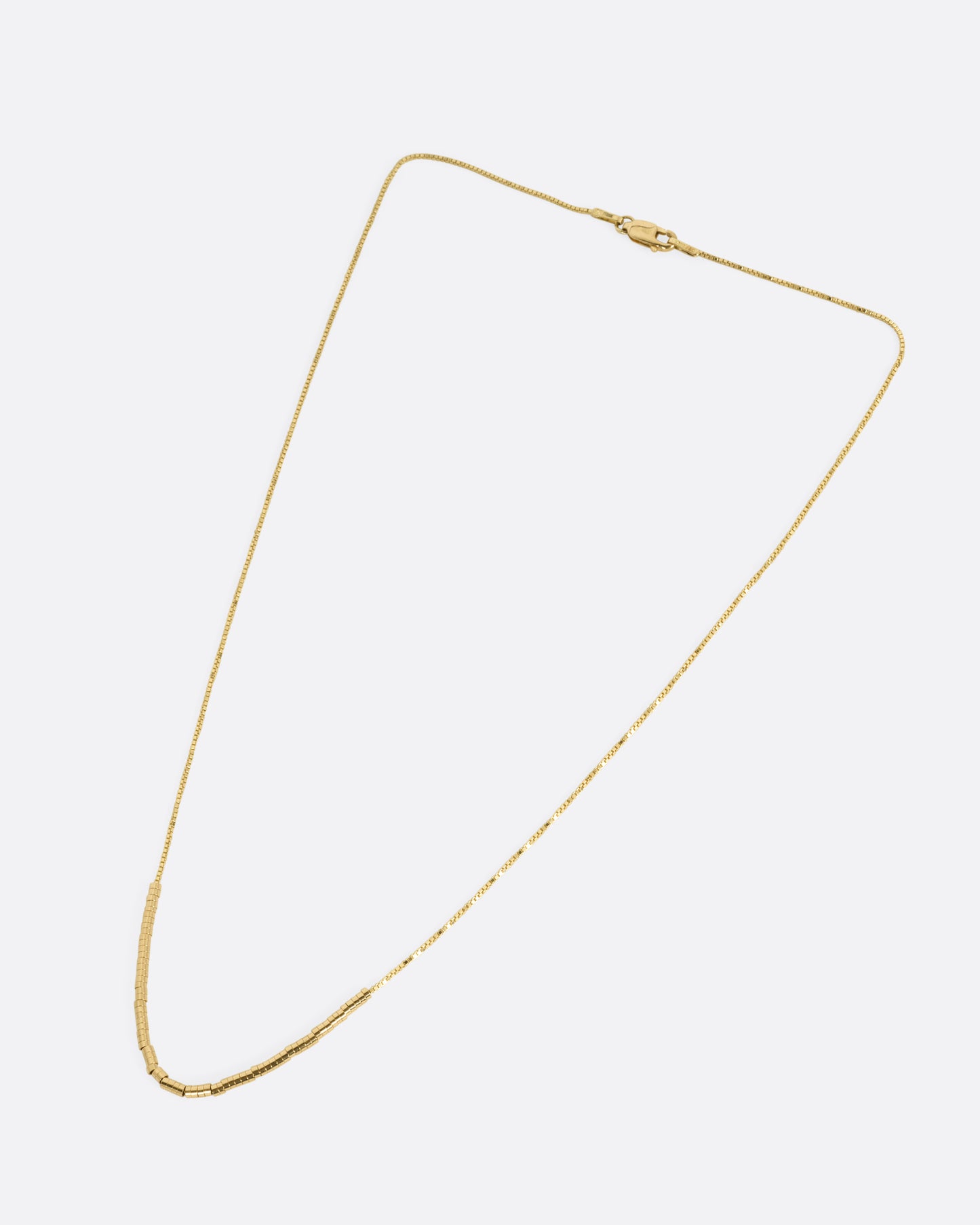 A yellow gold chain necklace with a queue of cylindrical gold beads, shown from the front.
