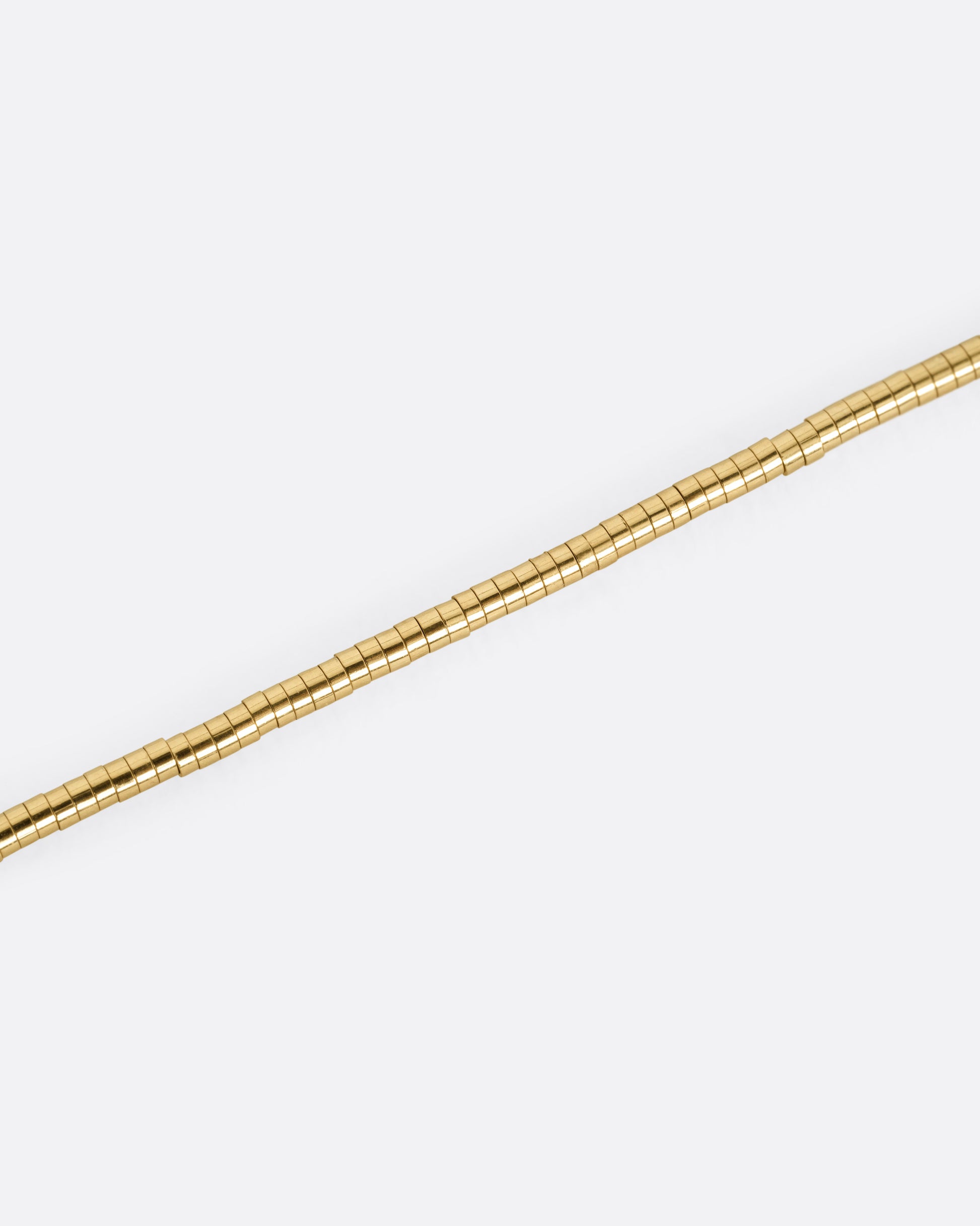 A close up of a yellow gold chain necklace with a queue of cylindrical gold beads.