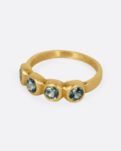 A yellow gold ring with four bezel set green sapphires, shown from the side.