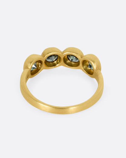 A yellow gold ring with four bezel set green sapphires, shown from the back.