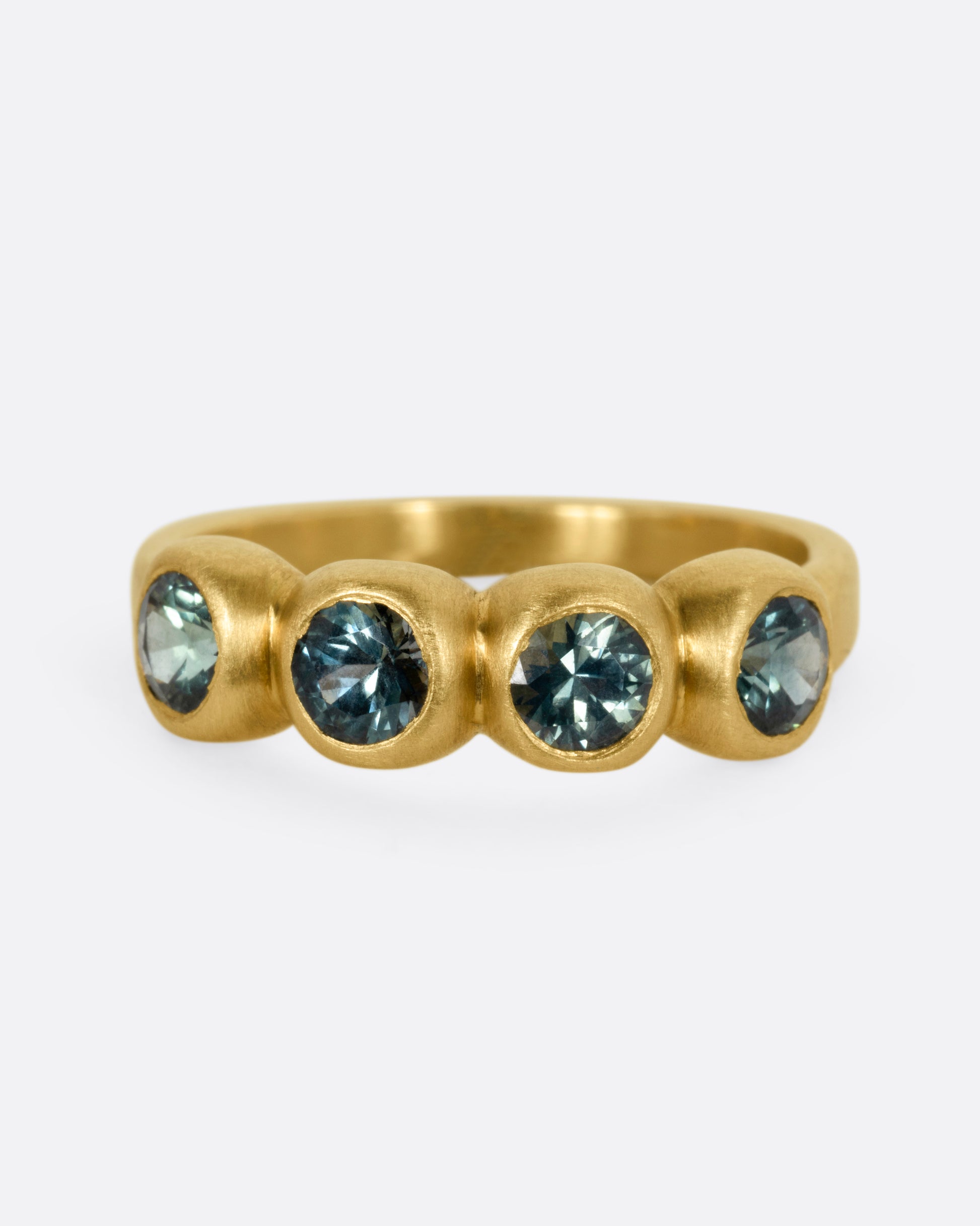 A yellow gold ring with four bezel set green sapphires, shown from the front.