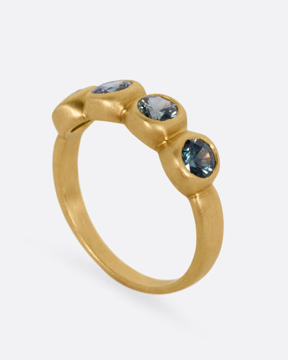 A yellow gold ring with four bezel set green sapphires, shown standing up from the side.