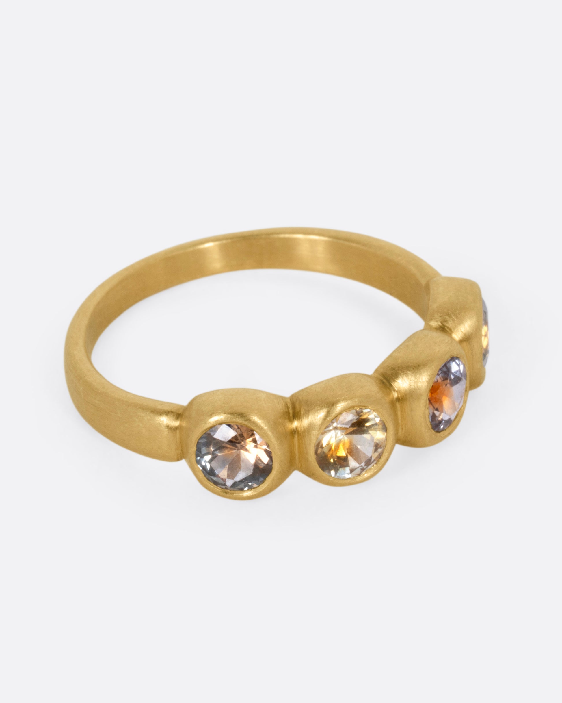 A yellow gold ring with four bezel set kaleidoscope sapphires, shown from the side.