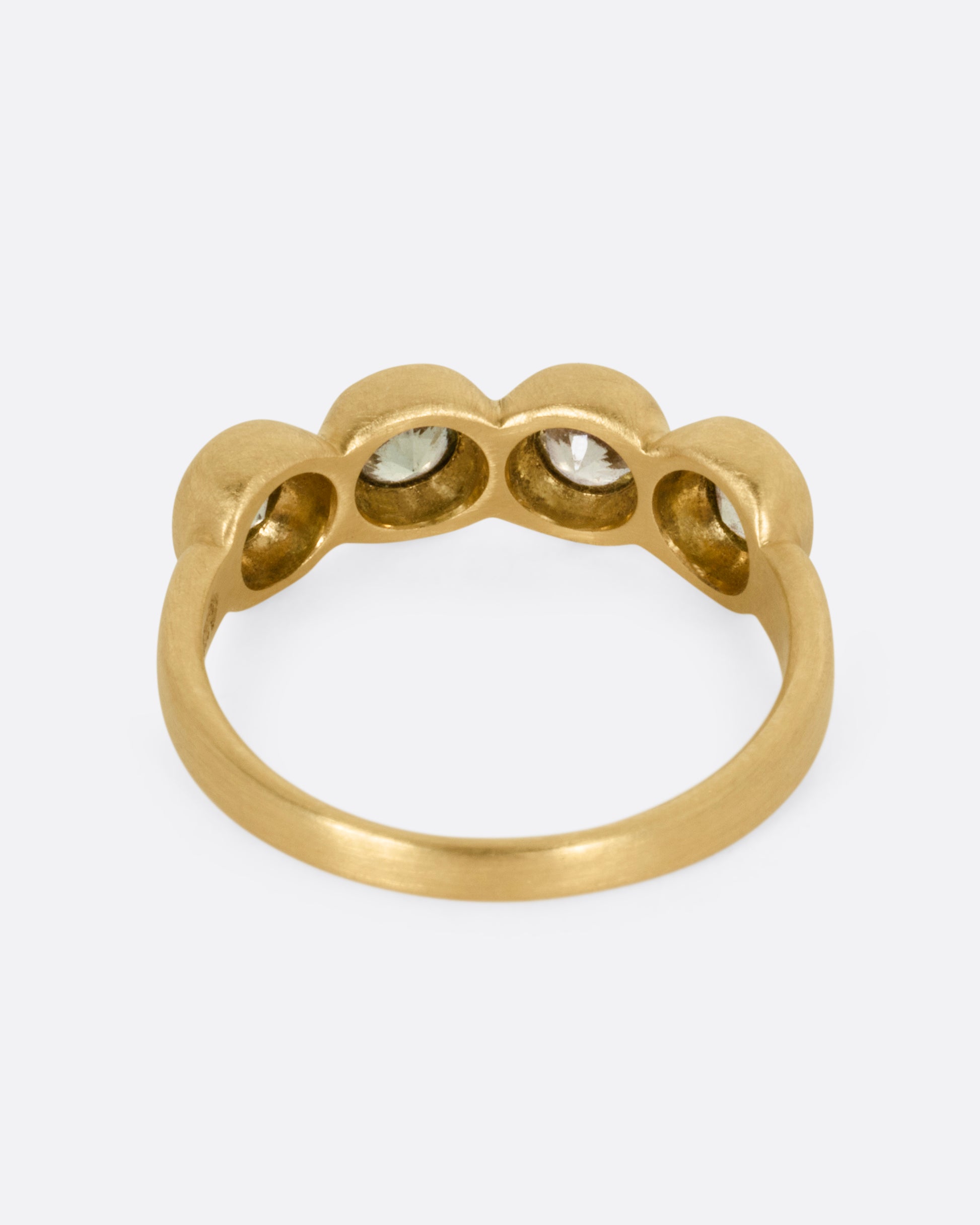 A yellow gold ring with four bezel set green sapphires, shown from the back.