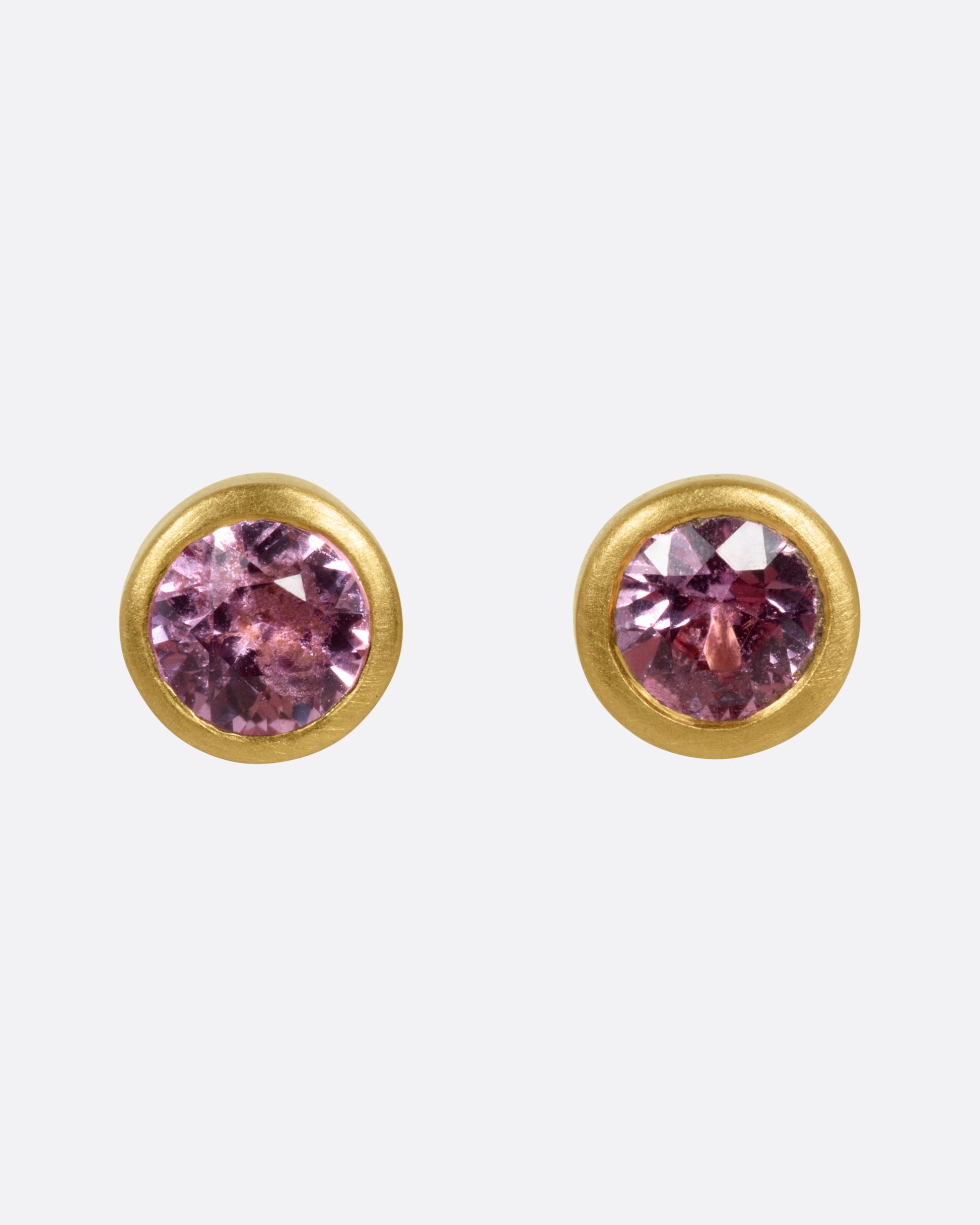 A pair of yellow gold stud earrings with pink sapphires, shown from the front.