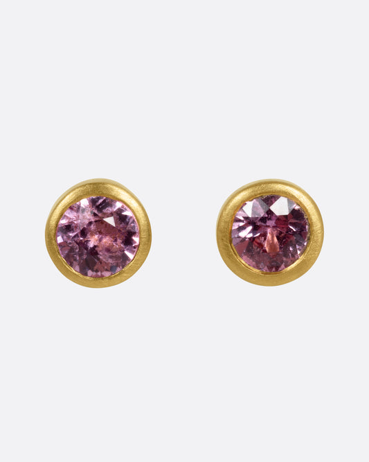 A pair of yellow gold stud earrings with pink sapphires, shown from the front.
