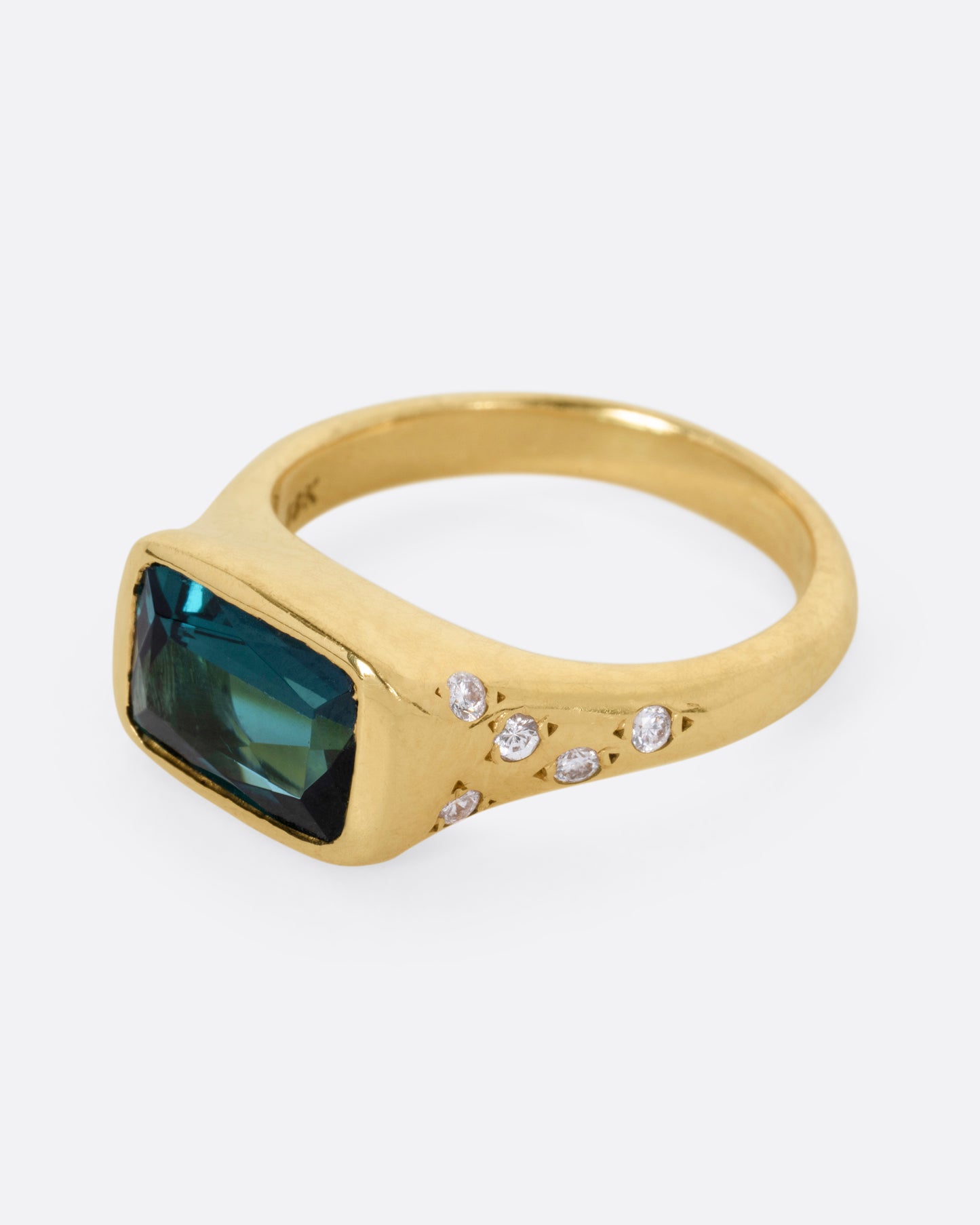 A yellow gold ring with a rectangular green tourmaline at the center and diamonds on either shoulder. Shown from the side.