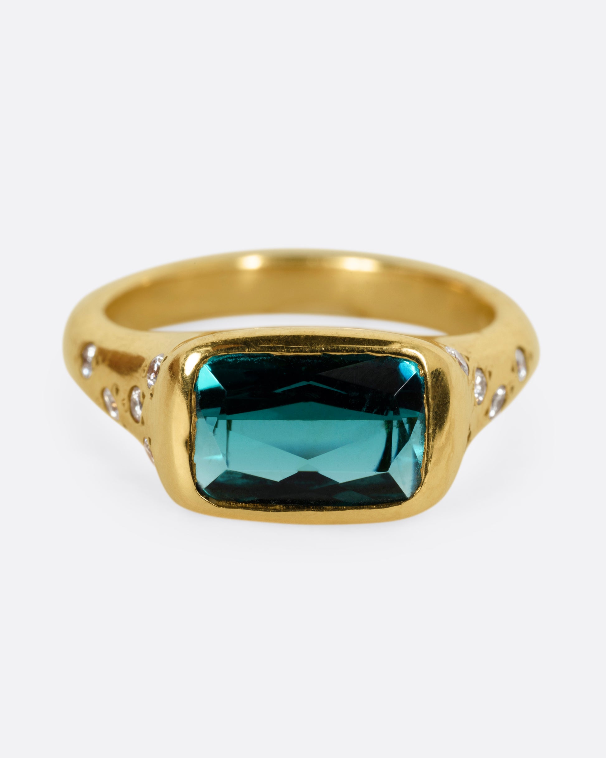 A yellow gold ring with a rectangular green tourmaline at the center and diamonds on either shoulder. Shown from the front. 