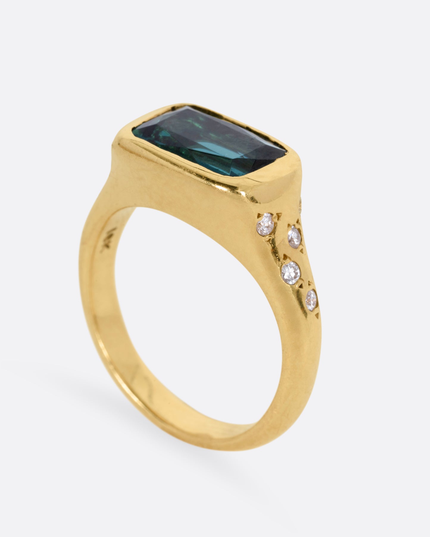 A yellow gold ring with a rectangular green tourmaline at the center and diamonds on either shoulder. Shown standing. 