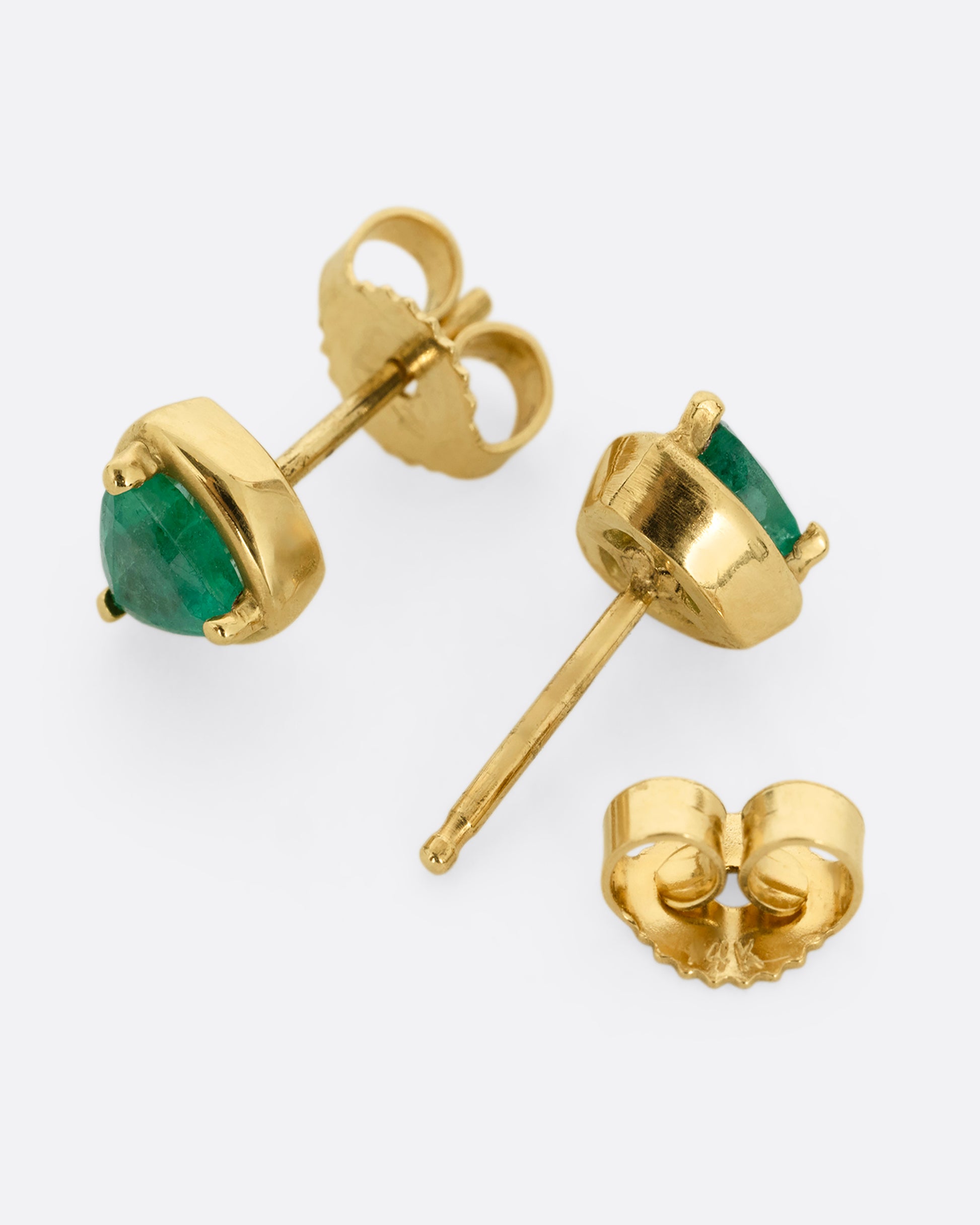 A pair of yellow gold stud earrings with emeralds. Shown lying flat from the side; one from the front, one open from the back.