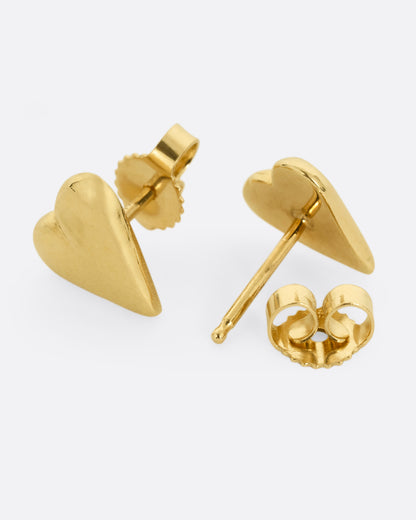 A pair of yellow gold heart earrings. Shown lying on their sides; one from the front, the other open from the back.