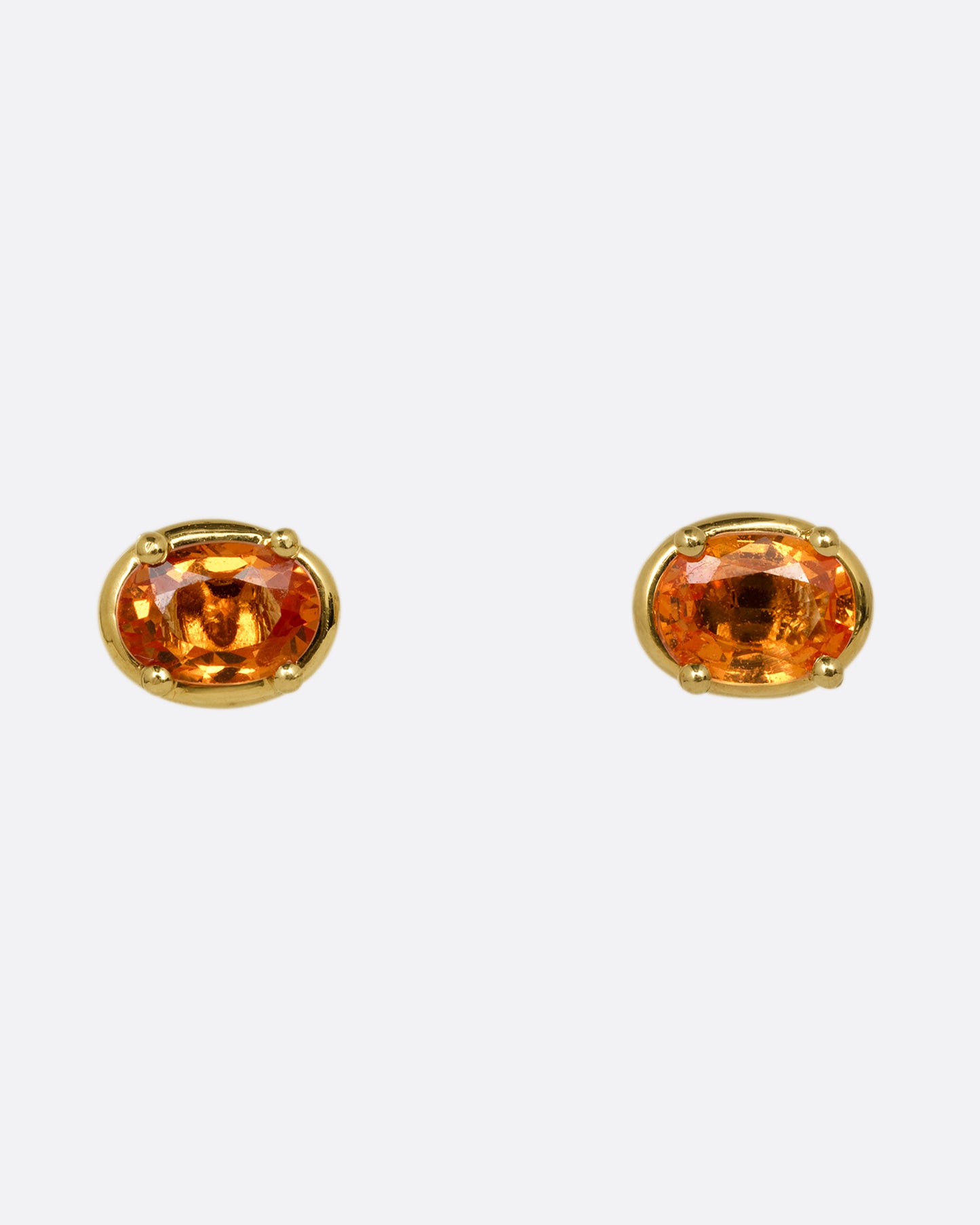A pair of yellow gold stud earrings with orange sapphires. Shown from the front.
