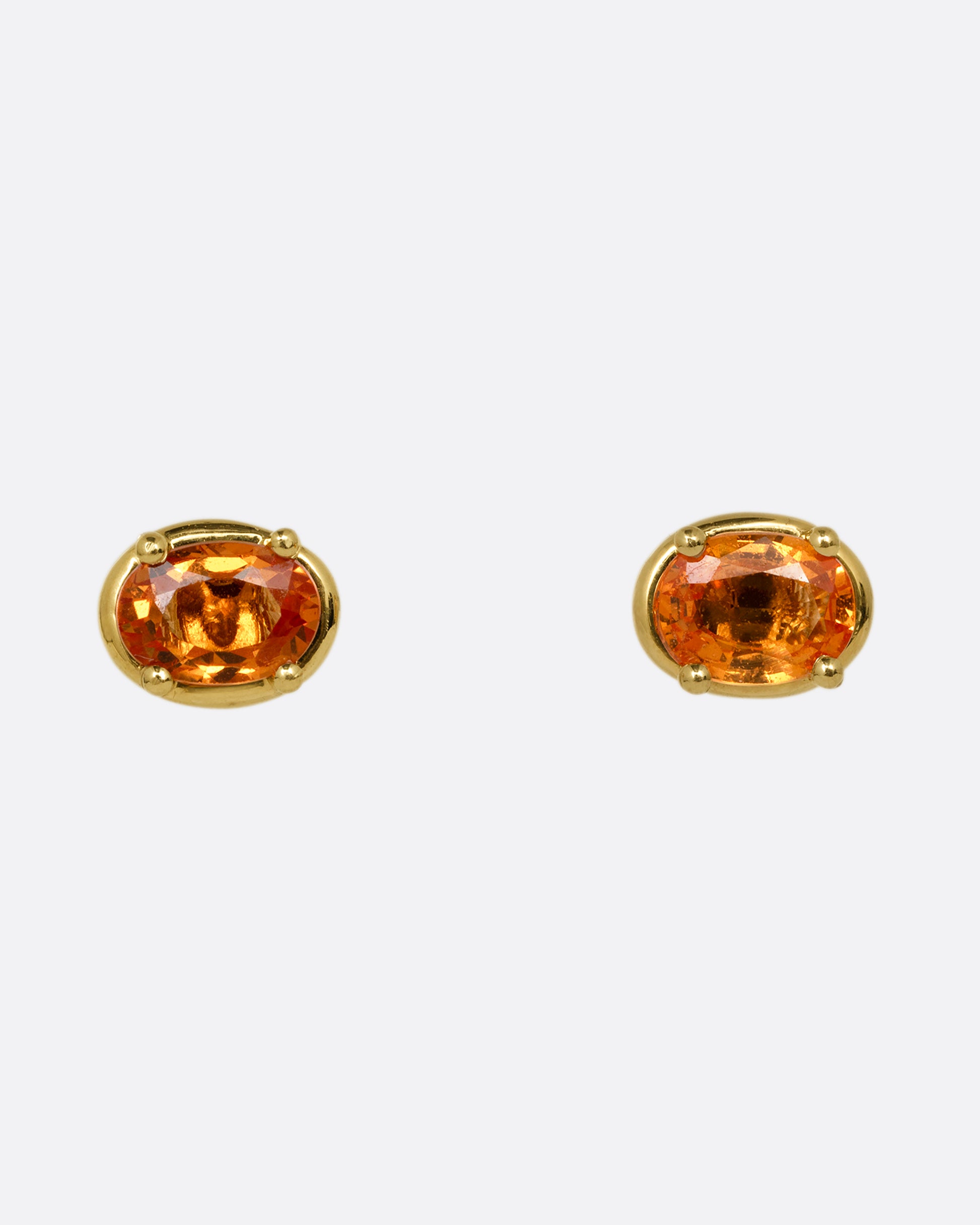 A pair of yellow gold stud earrings with orange sapphires. Shown from the front.