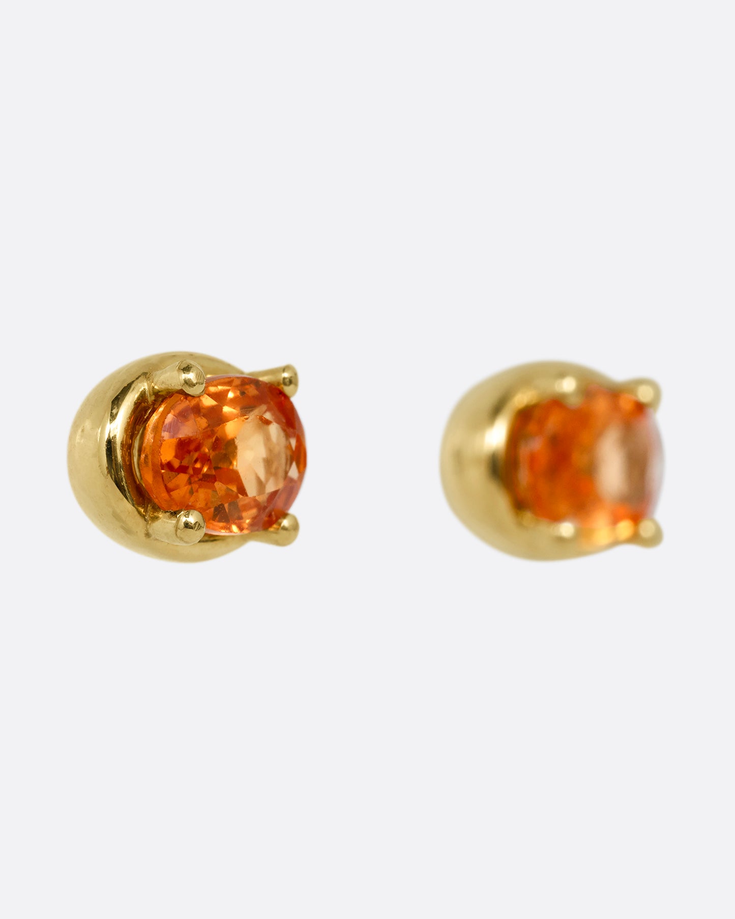 A pair of yellow gold stud earrings with orange sapphires. Shown from the side.
