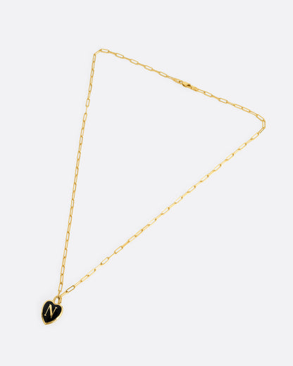 A yellow gold  paperclip chain necklace with a black enamel heart shaped N pendant. Shown closed lying flat at an angle from the front.